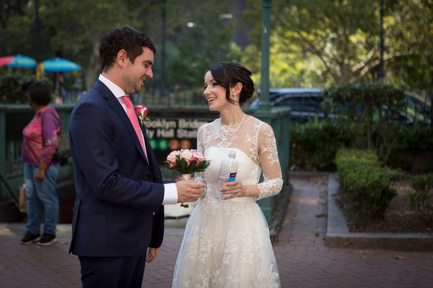 Bride in lace gown and groom in navy suit share a joyful moment near Brooklyn Bridge Park on their wedding day.