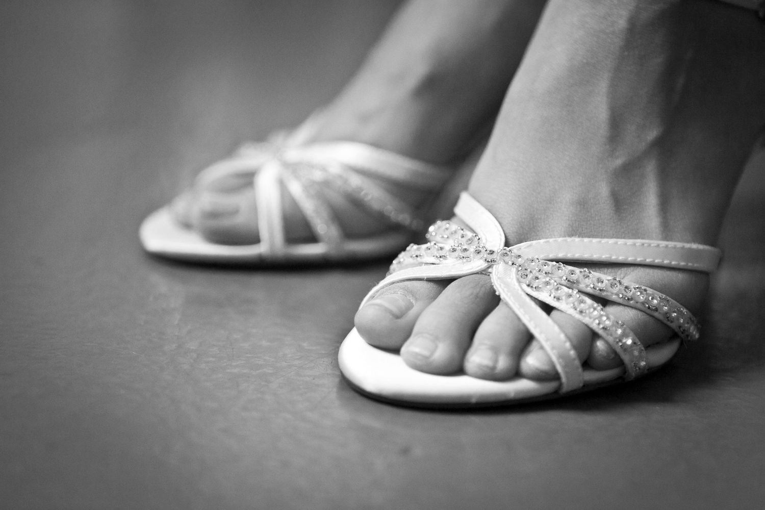 Black and white close-up of bridal sandals with rhinestone bow detail on womans feet.