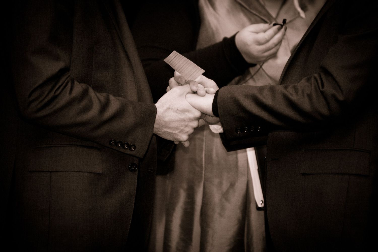 Close-up of two people holding hands and a book in sepia tone.