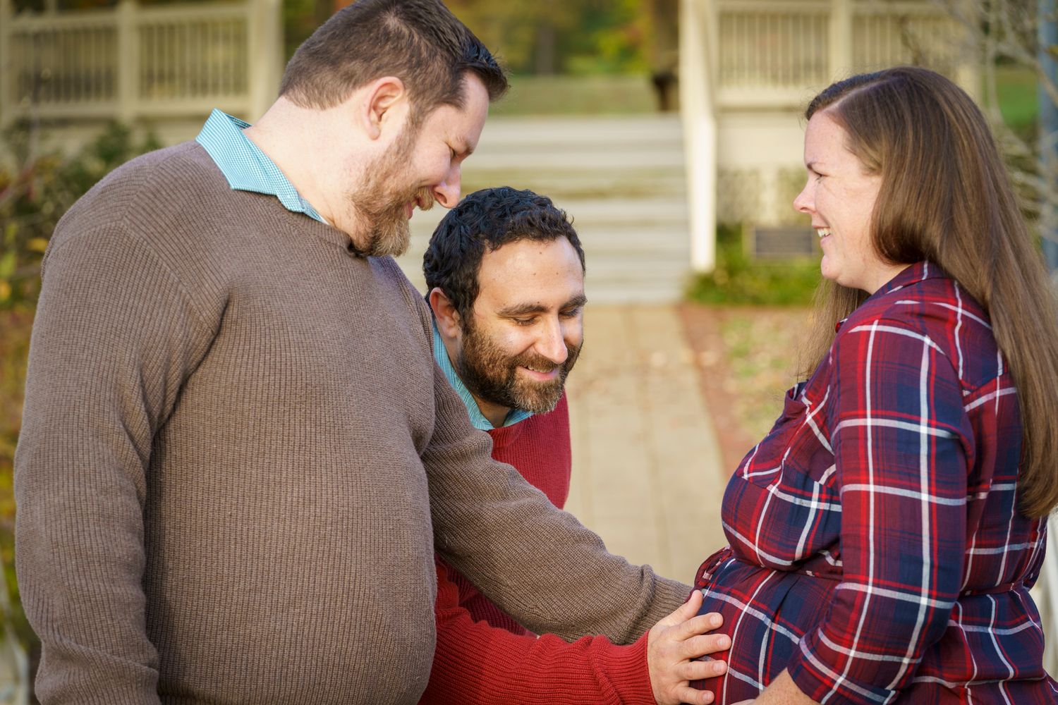 Two men and a pregnant woman sharing a joyful moment outdoors in fall.