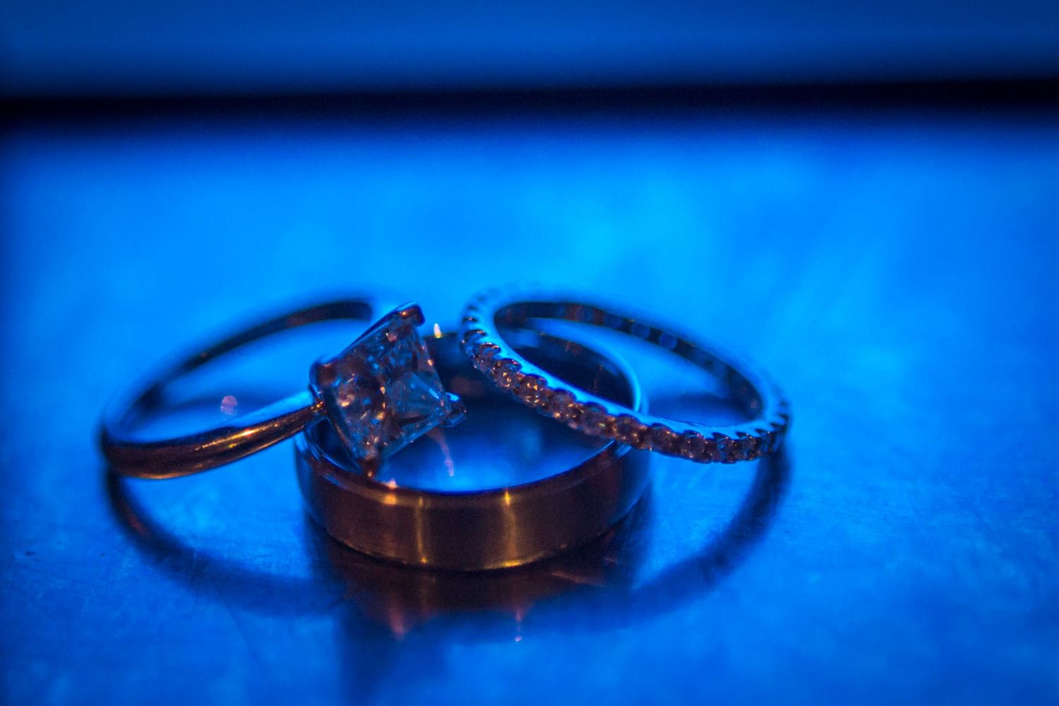 Three wedding rings elegantly arranged on a blue-lit surface showcasing diamond and gold bands.