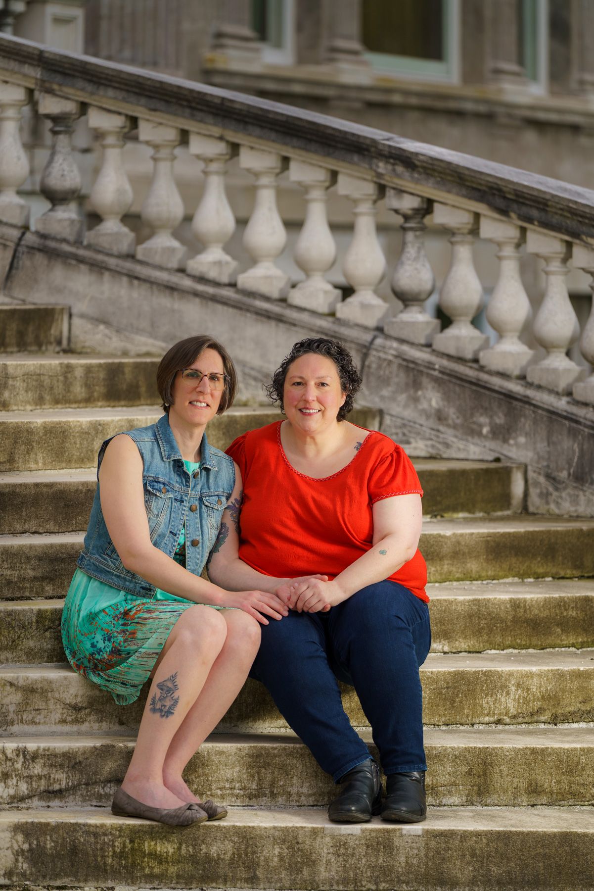 Two women sitting together on stone steps outside a historic building with ornate balustrade railing.