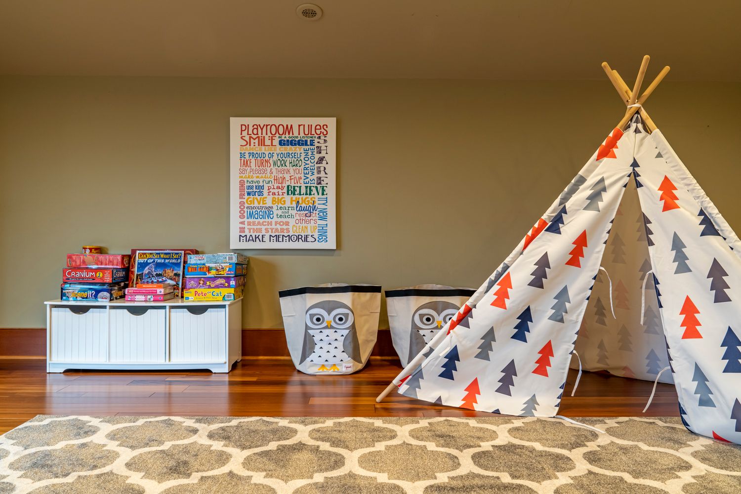 Colorful kids playroom with teepee tent, toy storage bins, and motivational poster on hardwood floors.