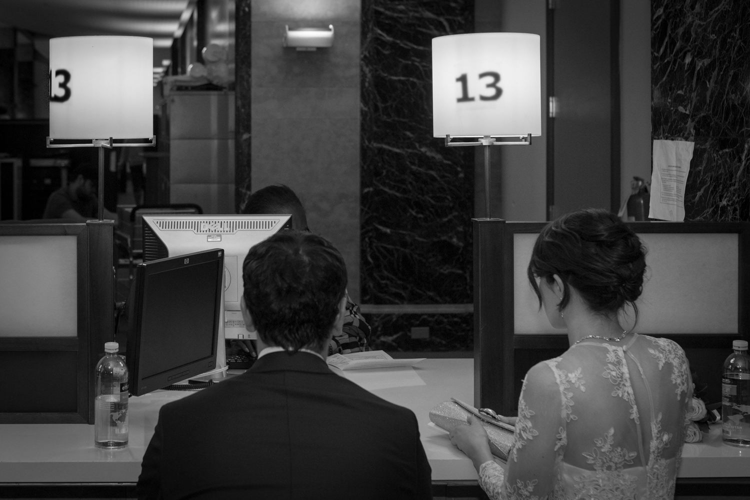 Black and white photo of a couple at table 13, woman checking phone, man in suit, formal setting.