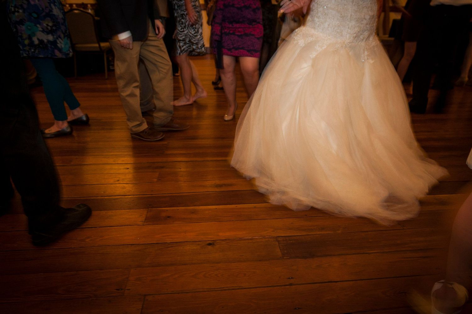 Bride twirling in flowing white tulle wedding gown on wooden dance floor at reception.