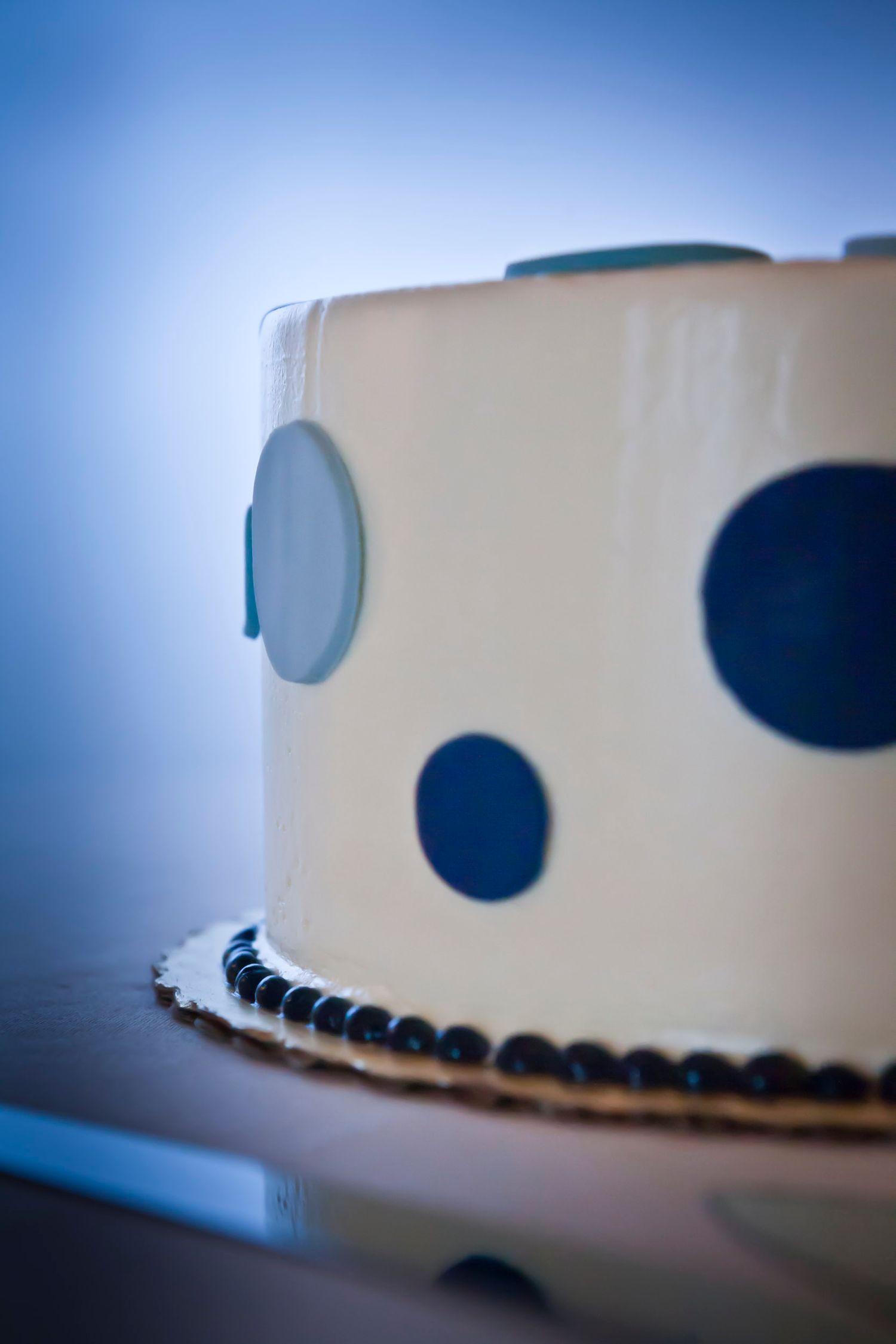 Elegant white wedding cake decorated with blue and navy polka dots on a light blue background.