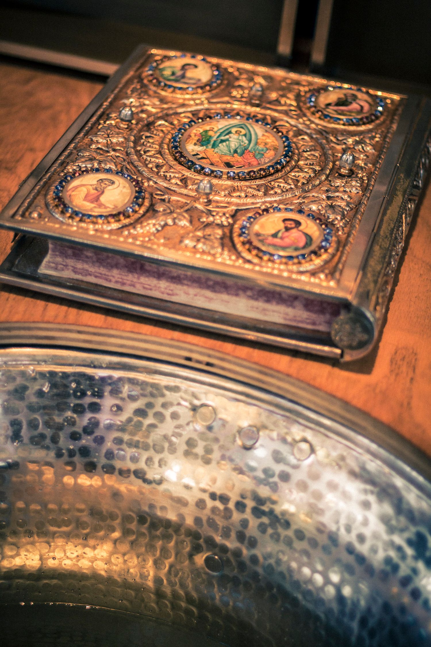 Ornate antique book with jeweled gold cover featuring religious medallions displayed on a wooden table.