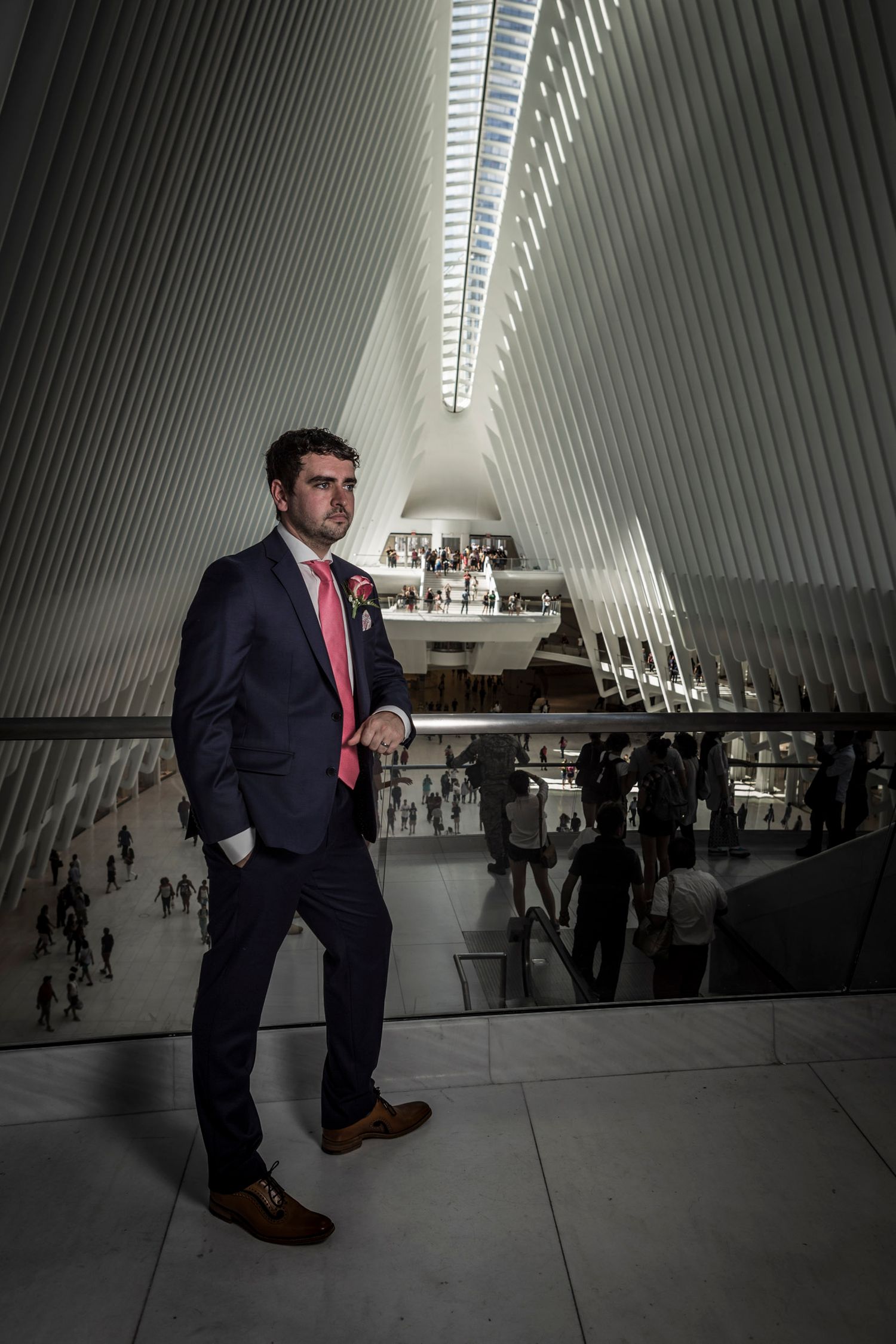 Groom in navy suit and pink tie poses inside the Oculus at World Trade Center, NYC.