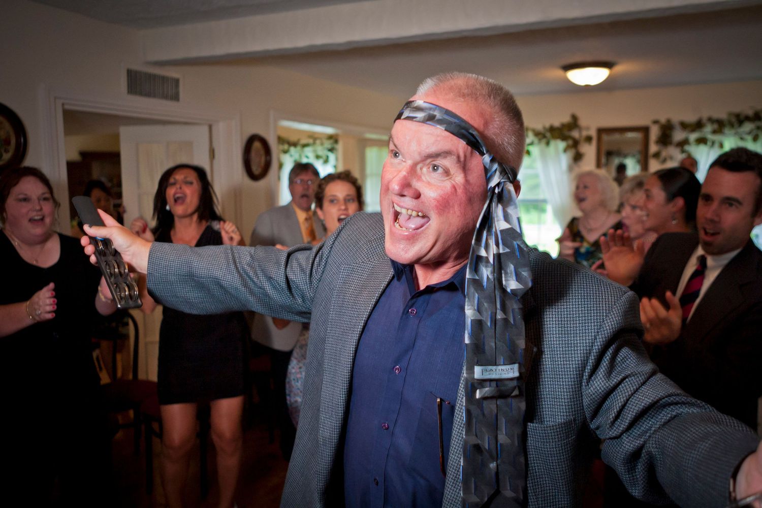 Energetic man dancing with scarf as blindfold at lively wedding reception party.