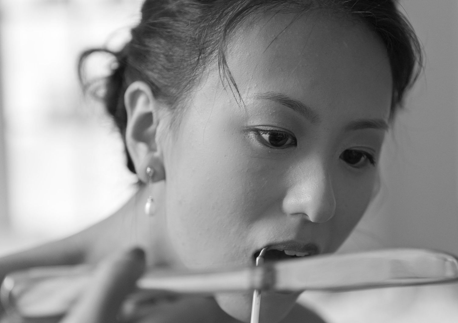 Black and white close-up portrait of a young Asian woman playing a stringed instrument with focused expression.
