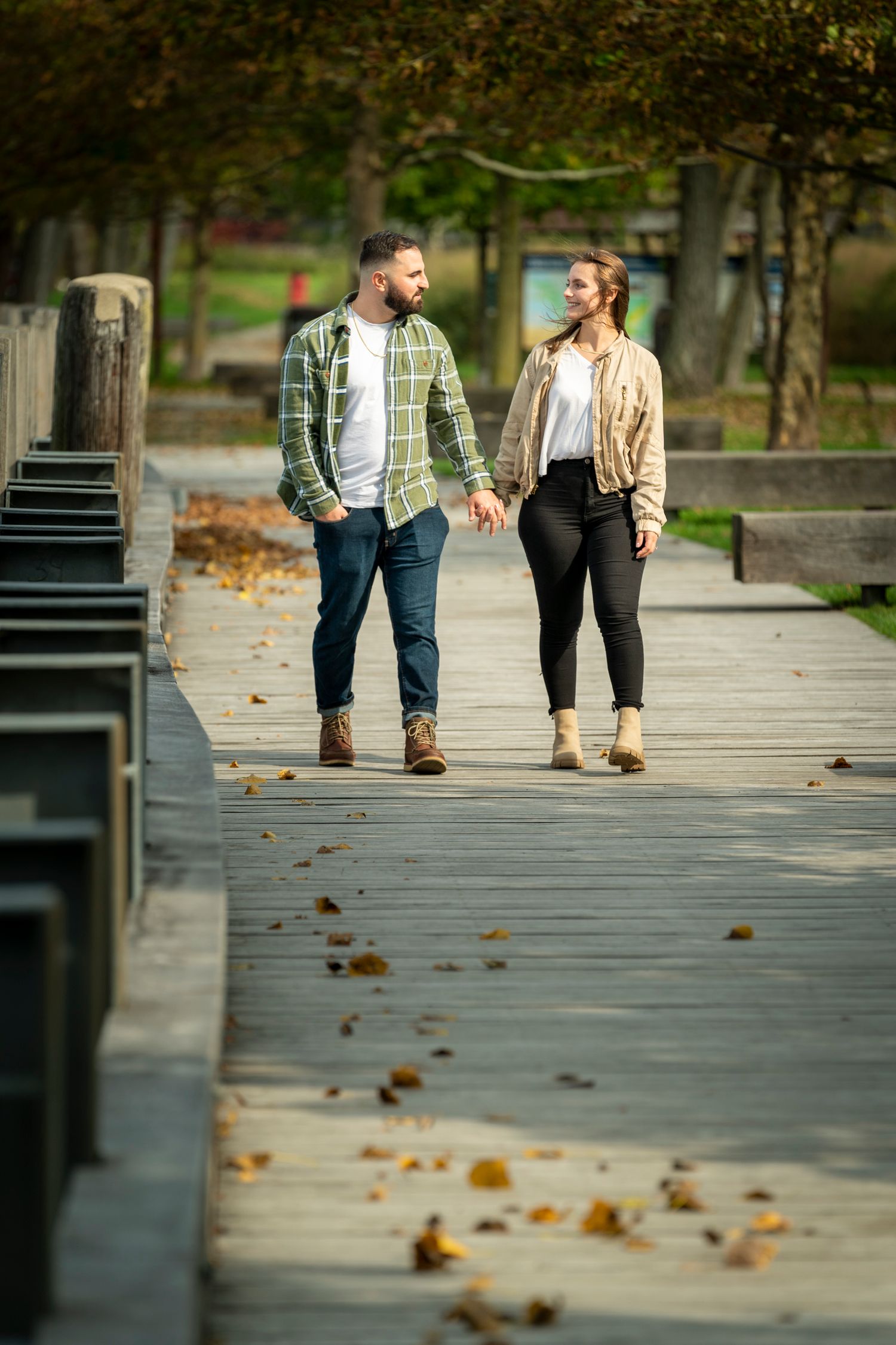 Couple holding hands walking on a wooden boardwalk path in an autumn park with fallen leaves.