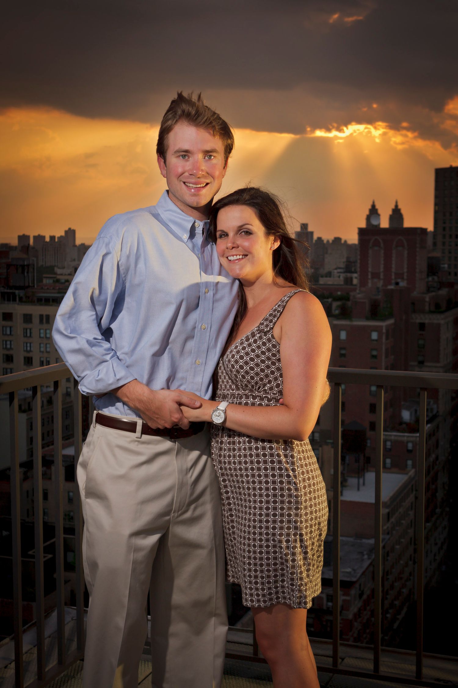 Couple standing together on a rooftop terrace with a dramatic golden sunset city skyline.