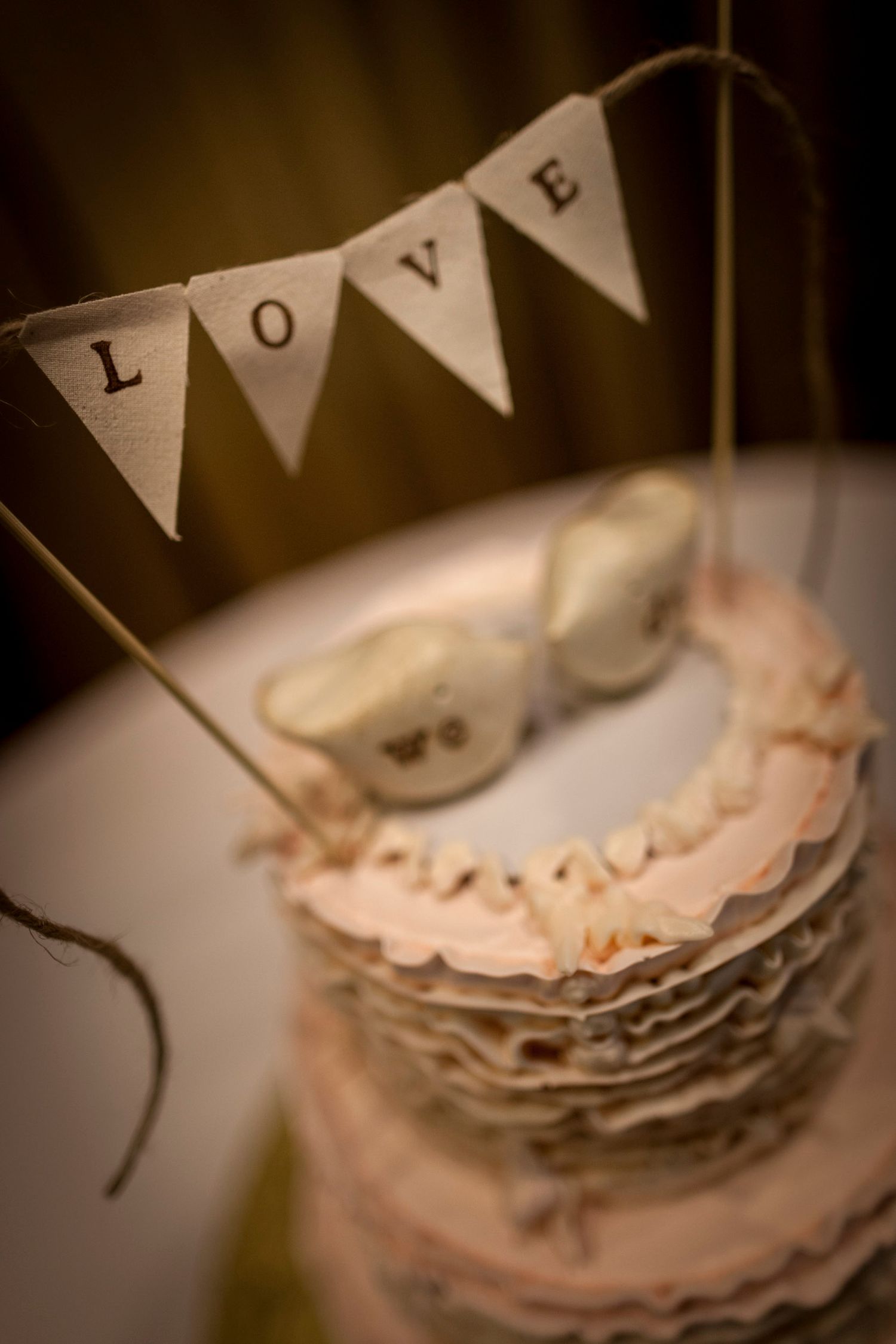 Elegant wedding cake with ruffled tiers, bird cake toppers, and a rustic LOVE bunting banner decoration.