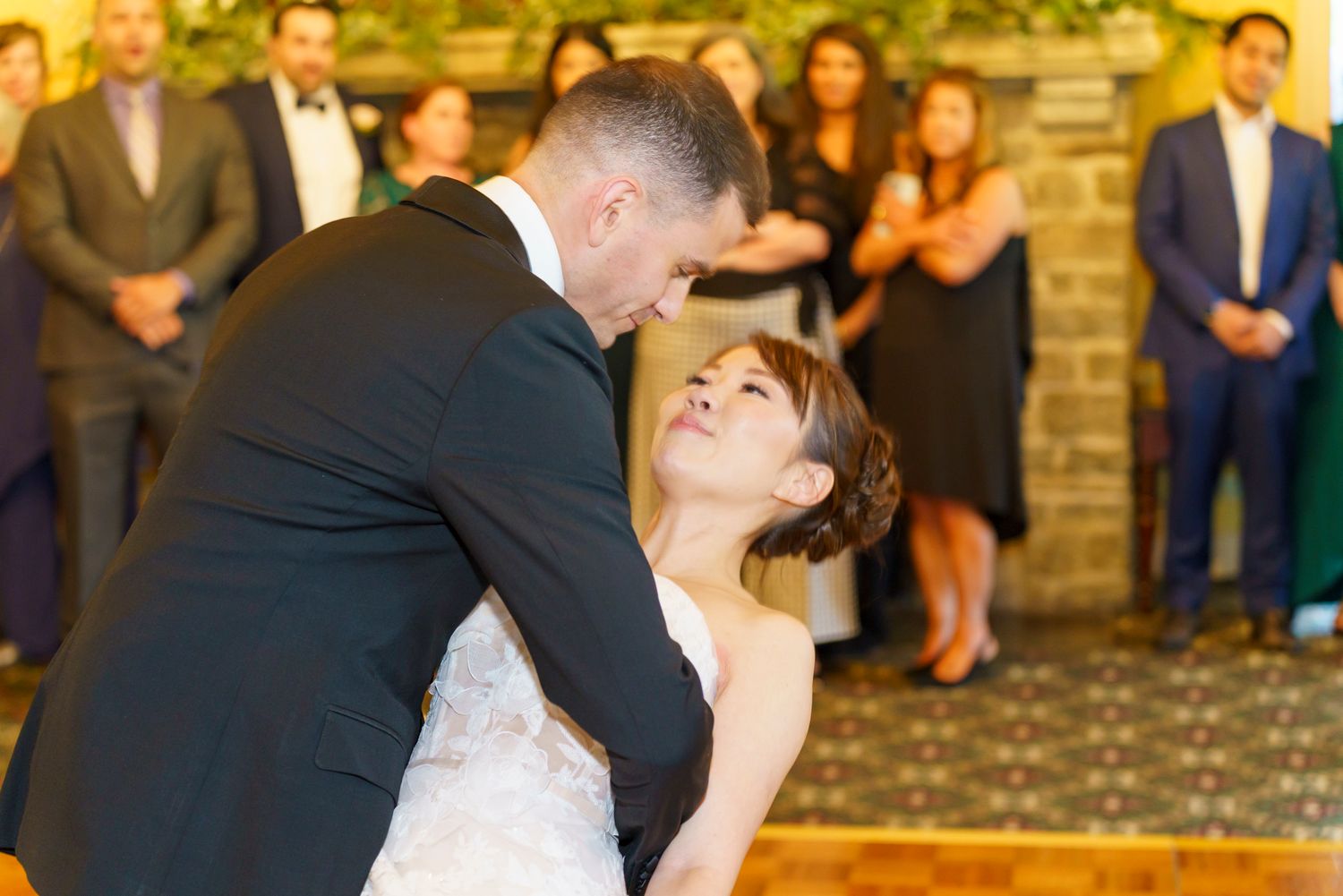 Bride and groom share their first dance at wedding reception, surrounded by guests watching the romantic moment.