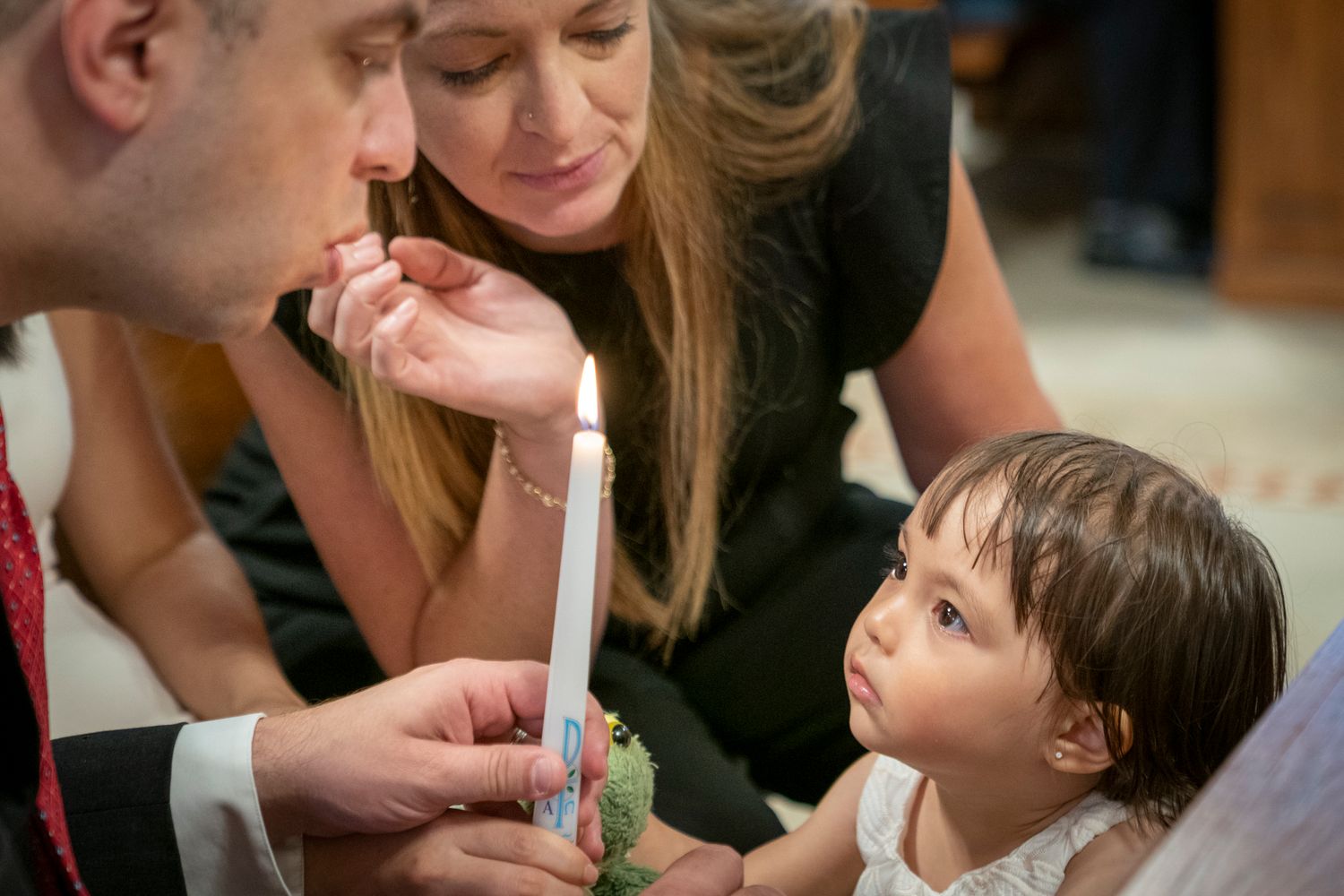 Parents and toddler girl watching a baptism candle being lit during a christening ceremony.