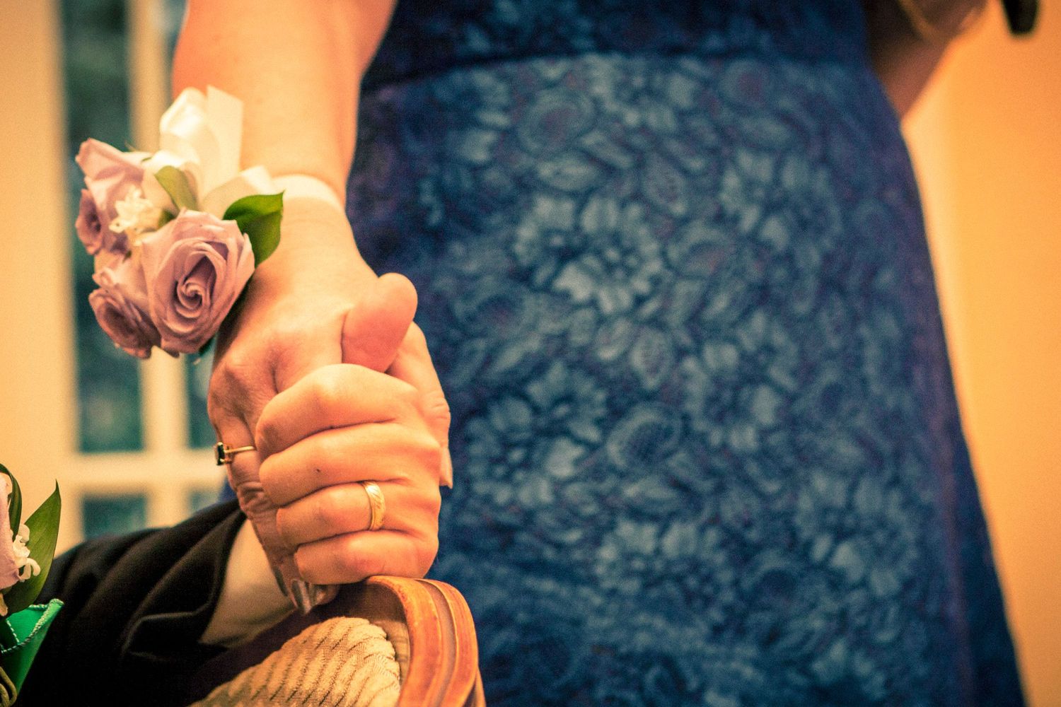 Close-up of two people holding hands with a pink rose corsage during a wedding ceremony.