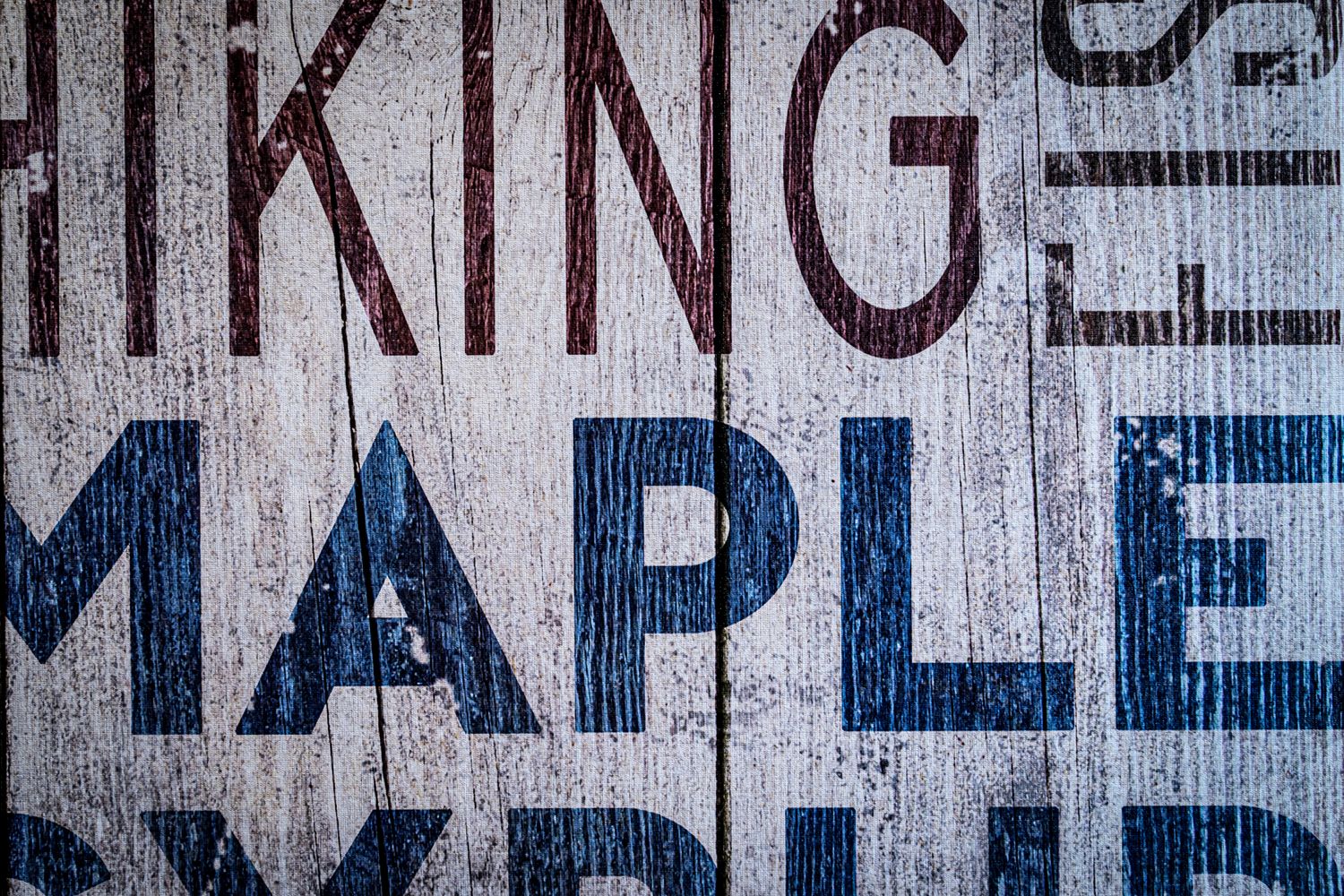 Rustic wooden sign with bold text reading Hiking and Maple Syrup in red and blue letters.