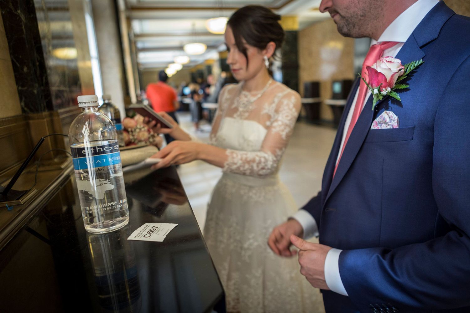 Bride and groom in wedding attire stand at a counter with a water bottle, celebrating their special day indoors.