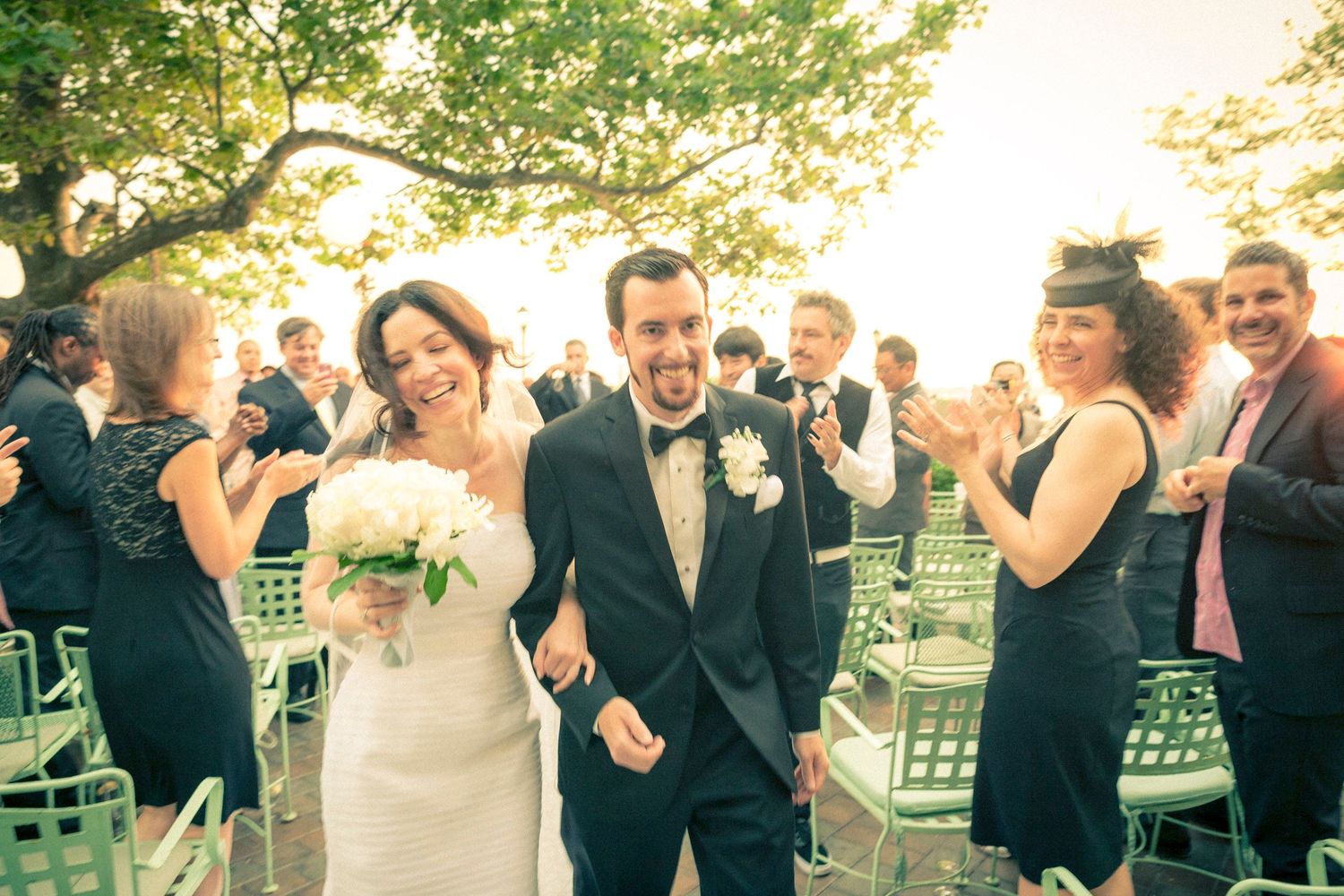 Happy newlywed couple walks back down the aisle as guests applaud outdoors.