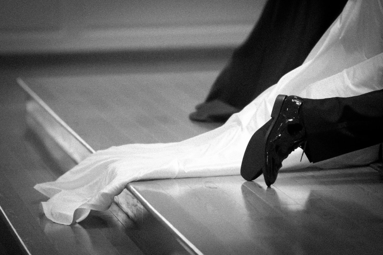 Black and white photo of bride's veil and groom's shoe at wedding altar.