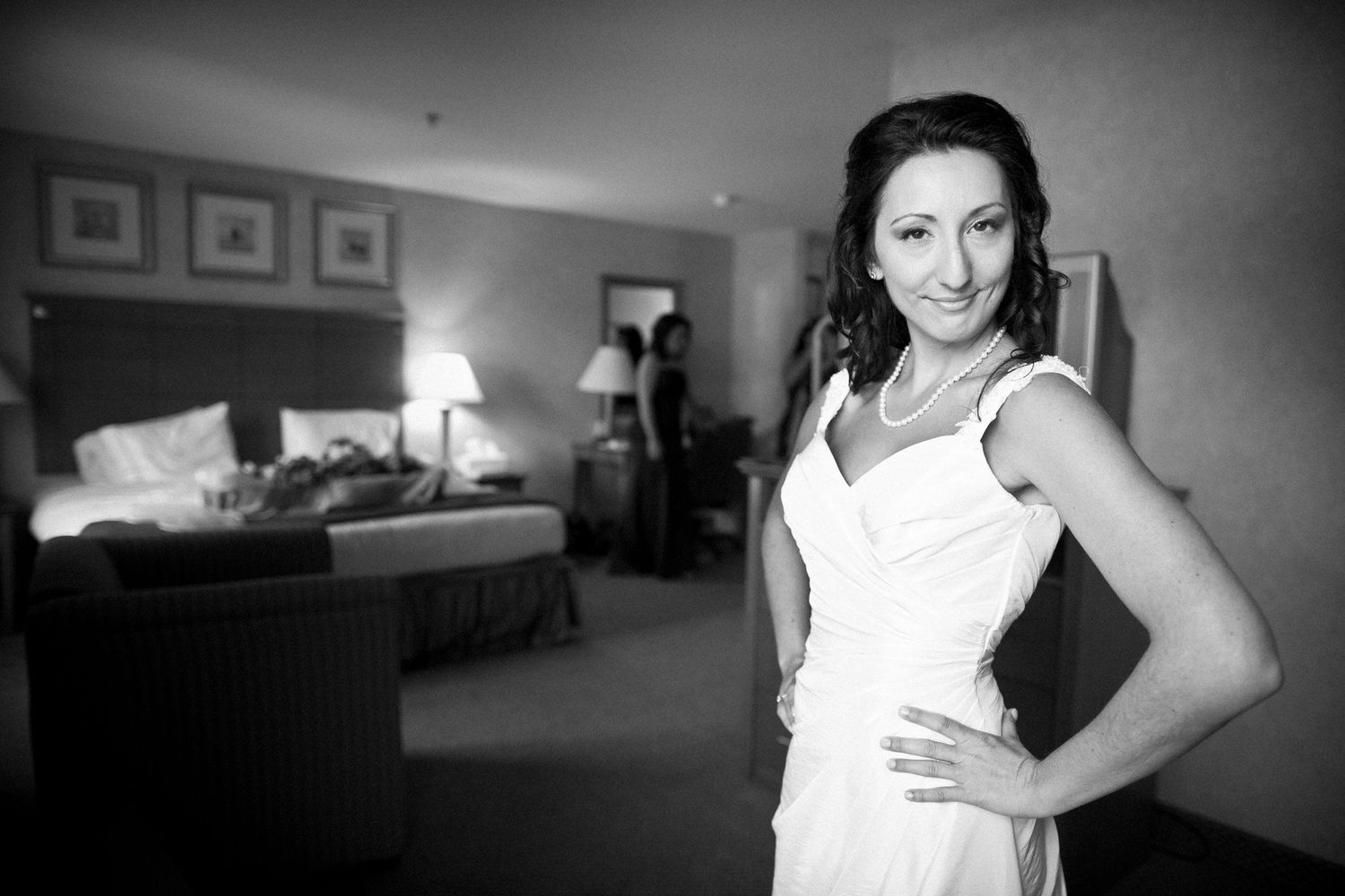 A bridesmaid in a white dress posing in a hotel room before the wedding.