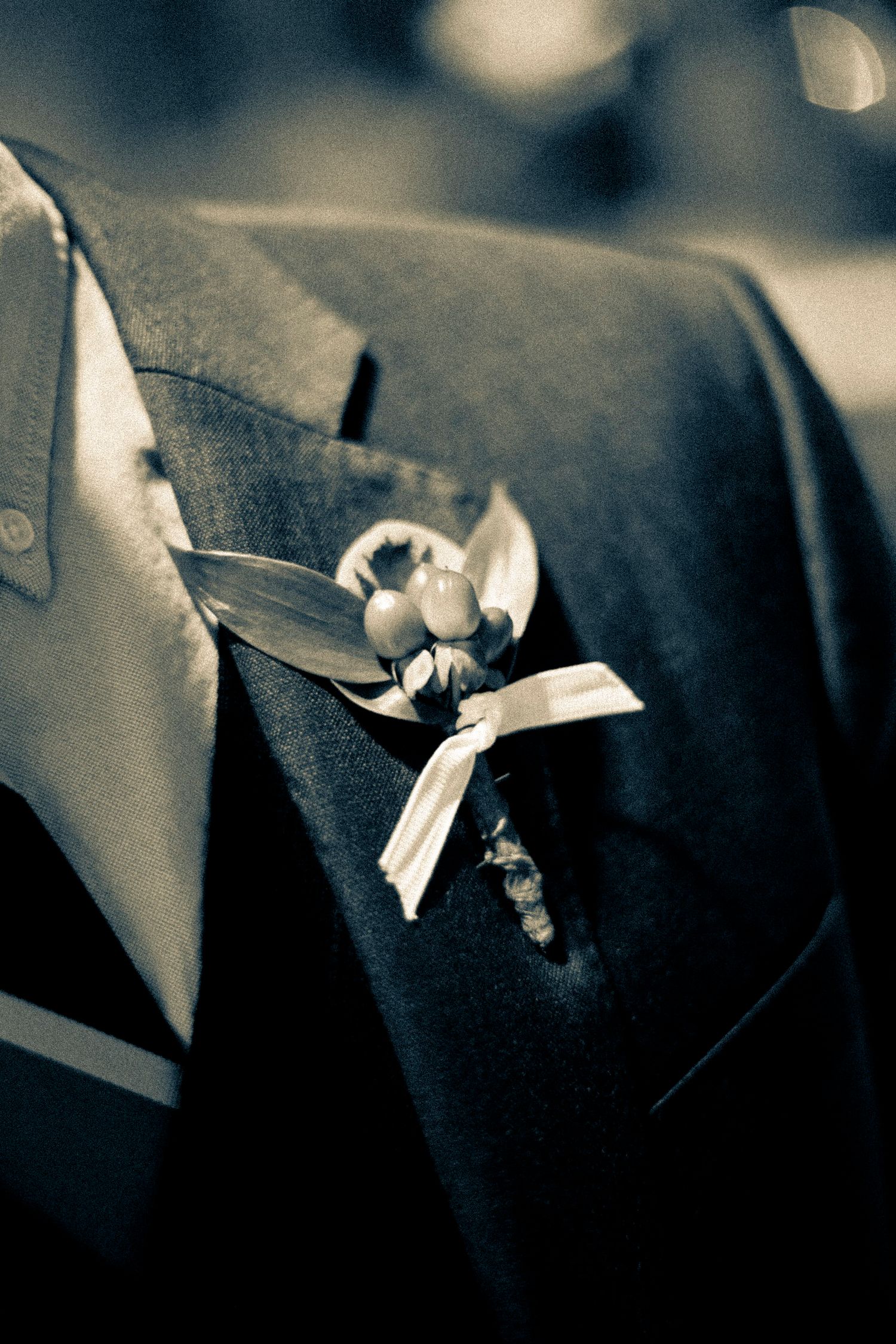 Close-up black and white photo of a floral boutonniere with berries on a suit lapel.