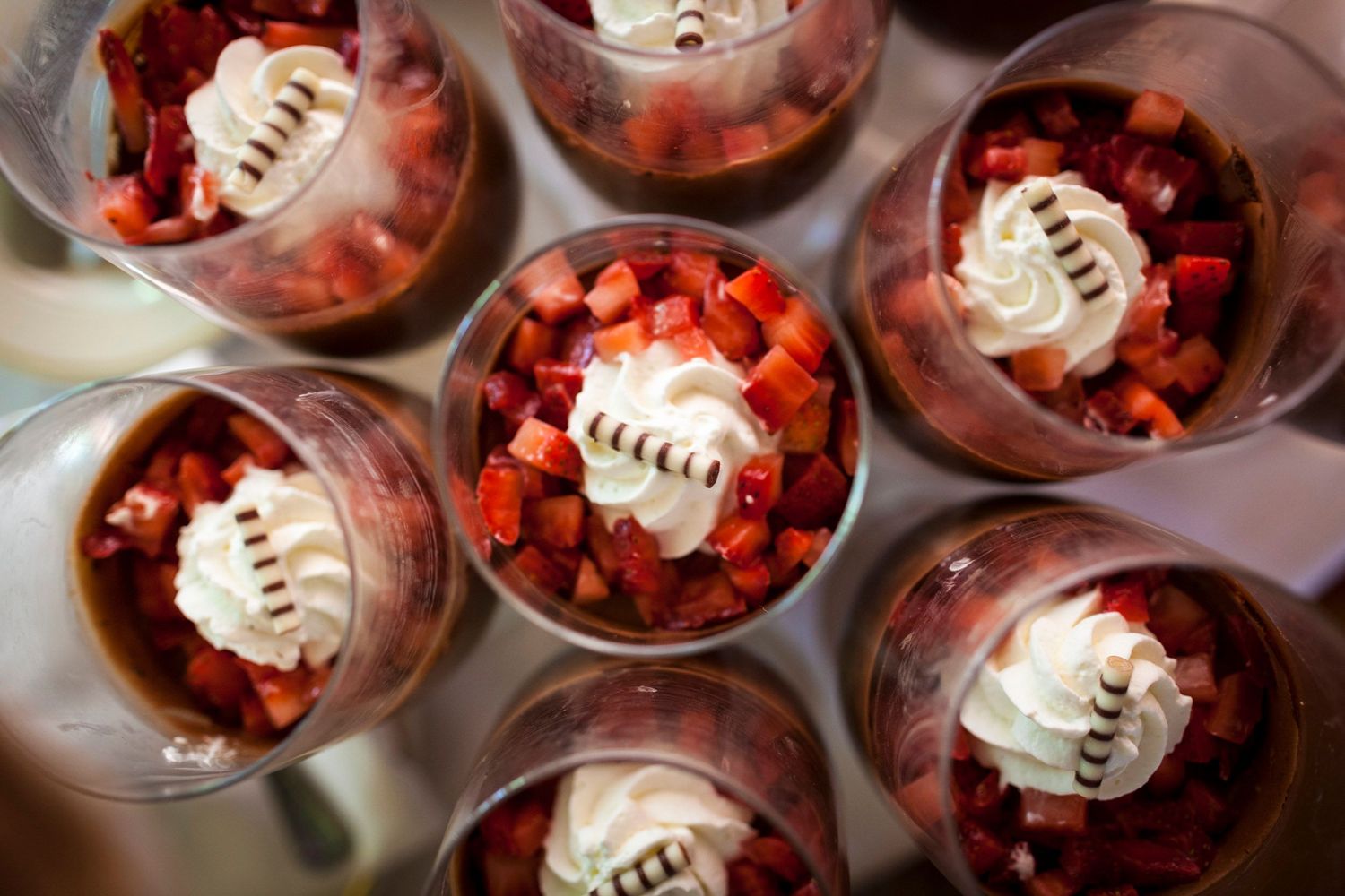 Overhead view of elegant dessert cups filled with fresh strawberries and whipped cream topping served at a catered event.