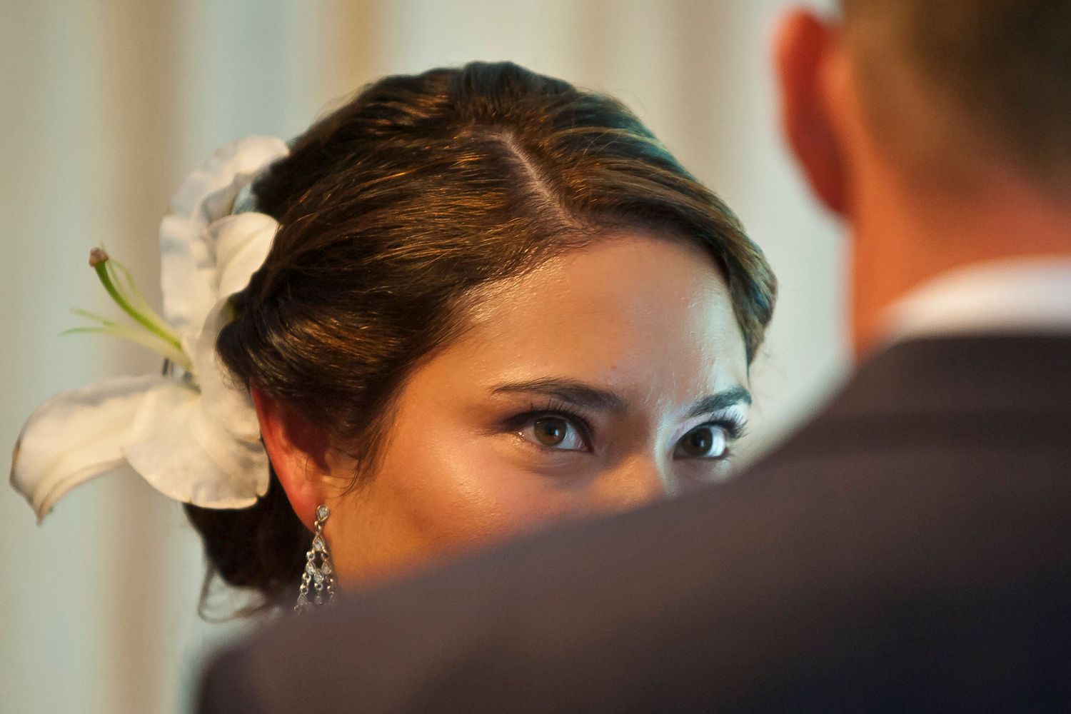 Close-up of a bride with a white flower in her hair gazing at her groom during the ceremony.
