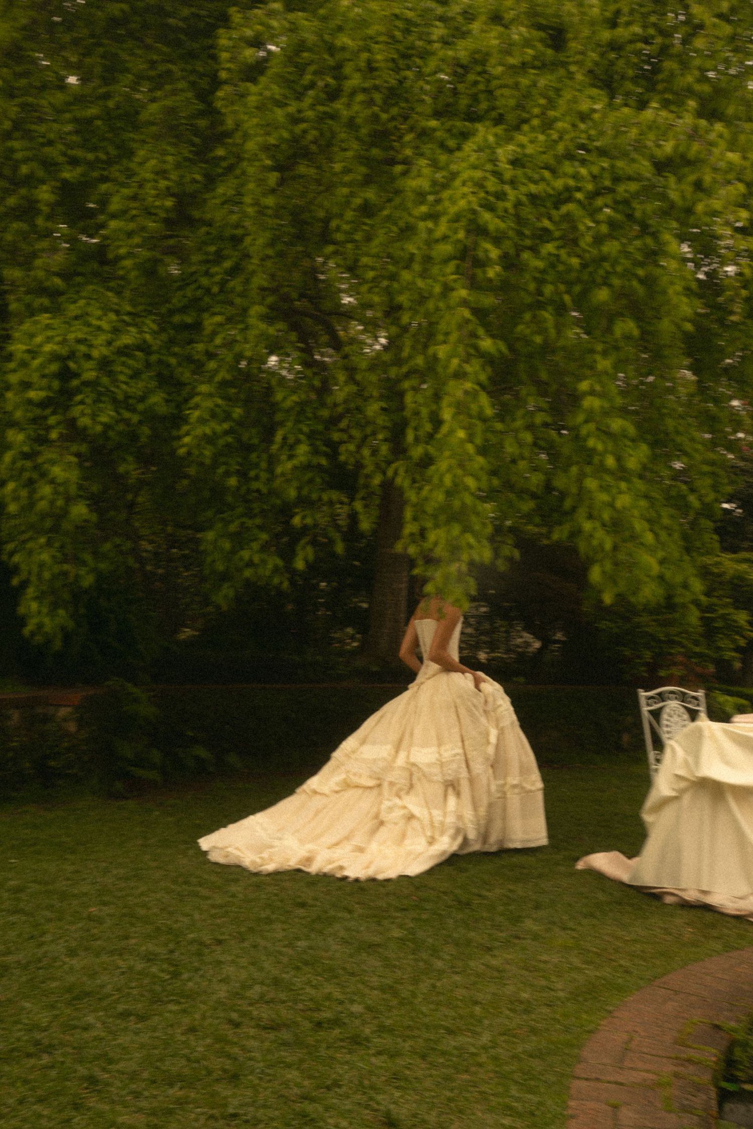 Bride in an elegant white ball gown standing beneath a large weeping willow tree outdoors.