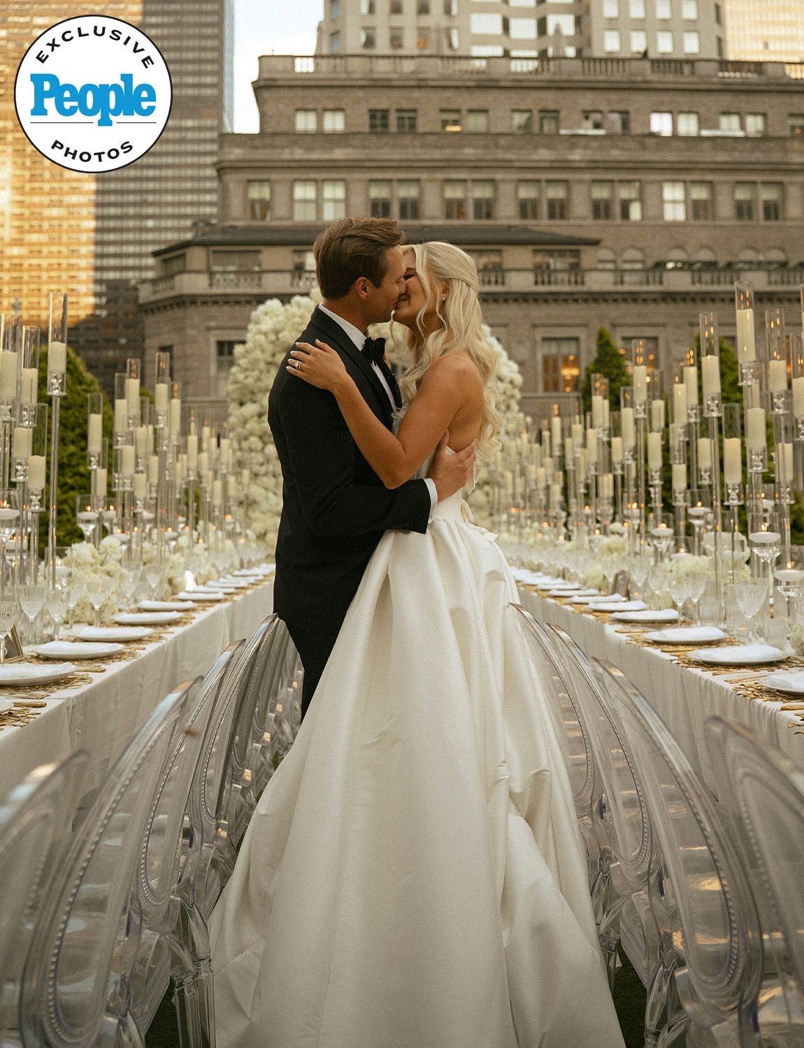 Featured in People magazine. Couple sharing a kiss at elegant outdoor wedding reception with tall candle centerpieces and city backdrop.