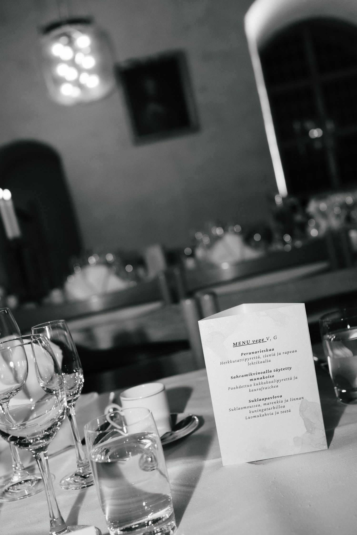 Black and white close-up of elegant table setting with wine glasses and menu card at formal dinner.