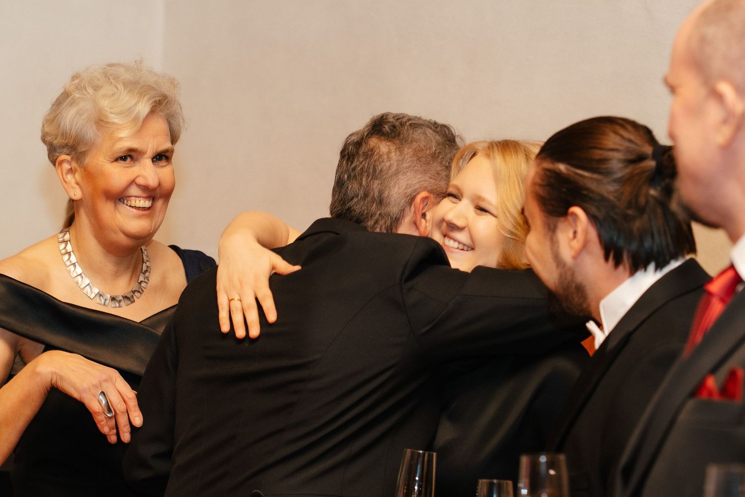 Guests in formal black attire sharing warm embrace at sophisticated evening gala celebration.