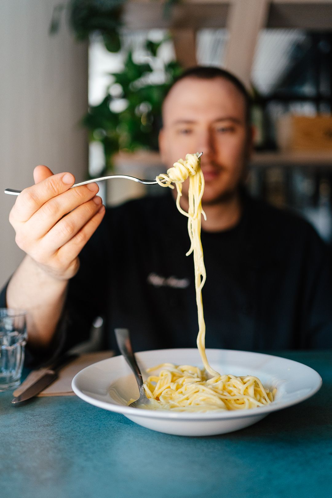 Chef twirling fresh spaghetti on a fork over a white bowl of pasta in a restaurant.