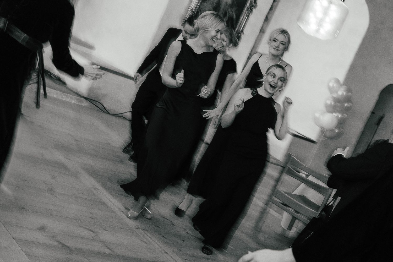 Black and white photo of women in black dresses dancing joyfully at formal event.