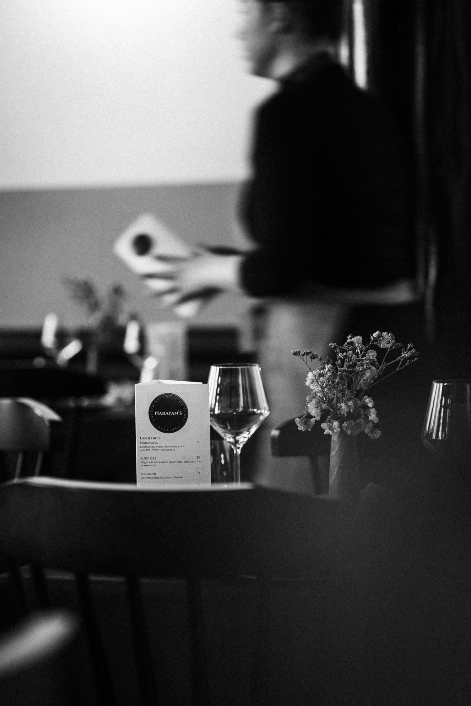 Black and white photo of a restaurant table with wine glass, menu, and floral centerpiece.