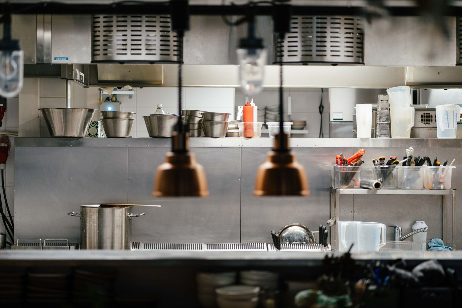 Professional restaurant kitchen with stainless steel shelving, copper pendant lights, and cooking equipment.
