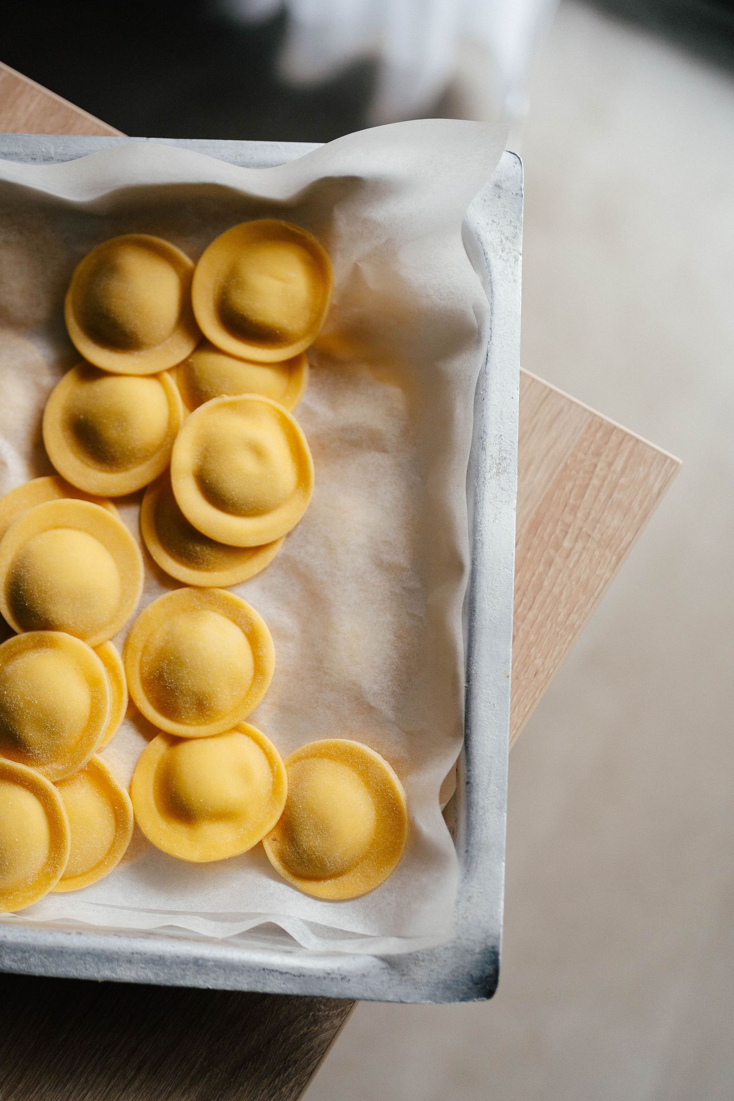 Fresh handmade tortellini pasta arranged on parchment paper in a wooden box.