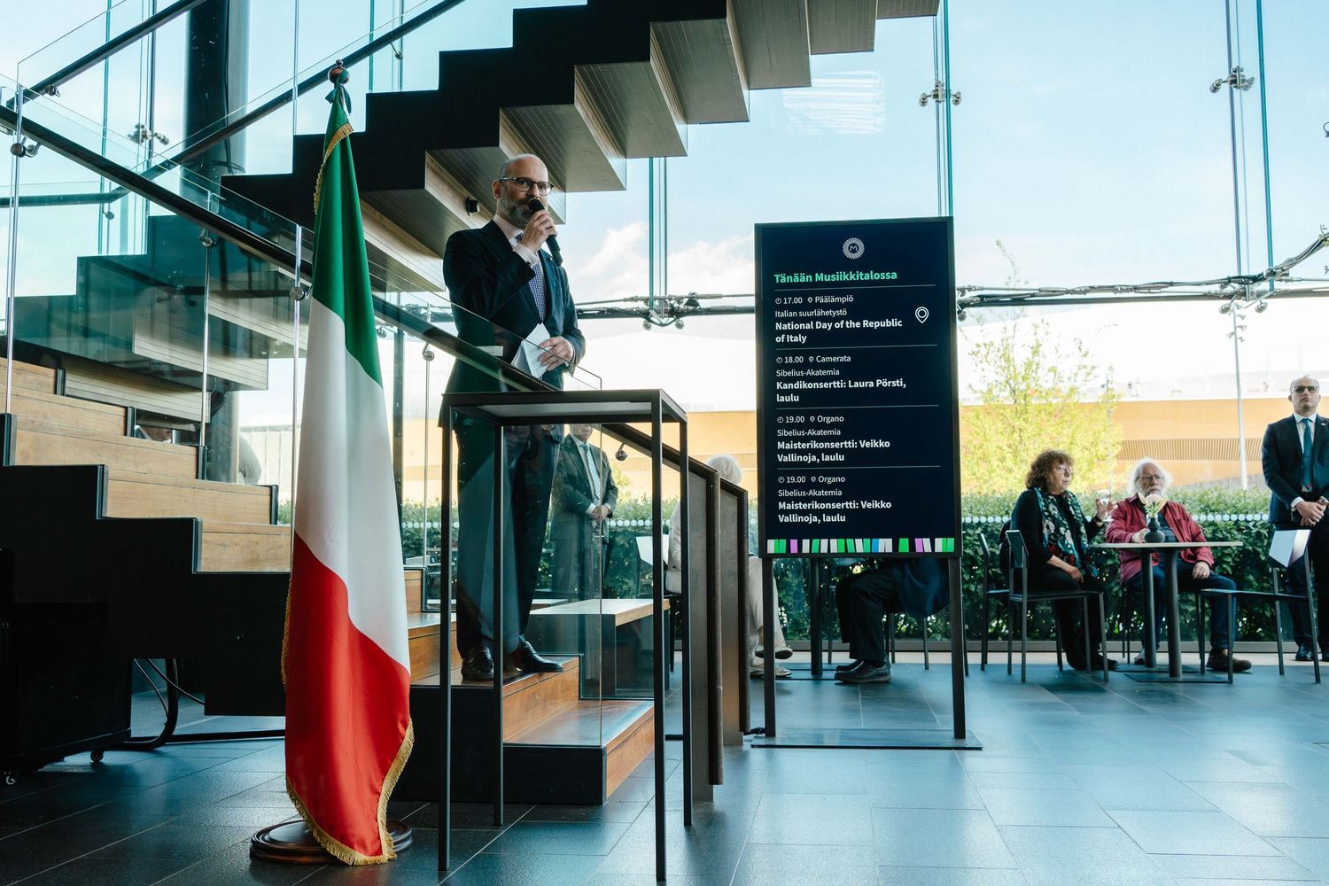 Speaker at podium with Italian flag during National Day of Italy ceremony.