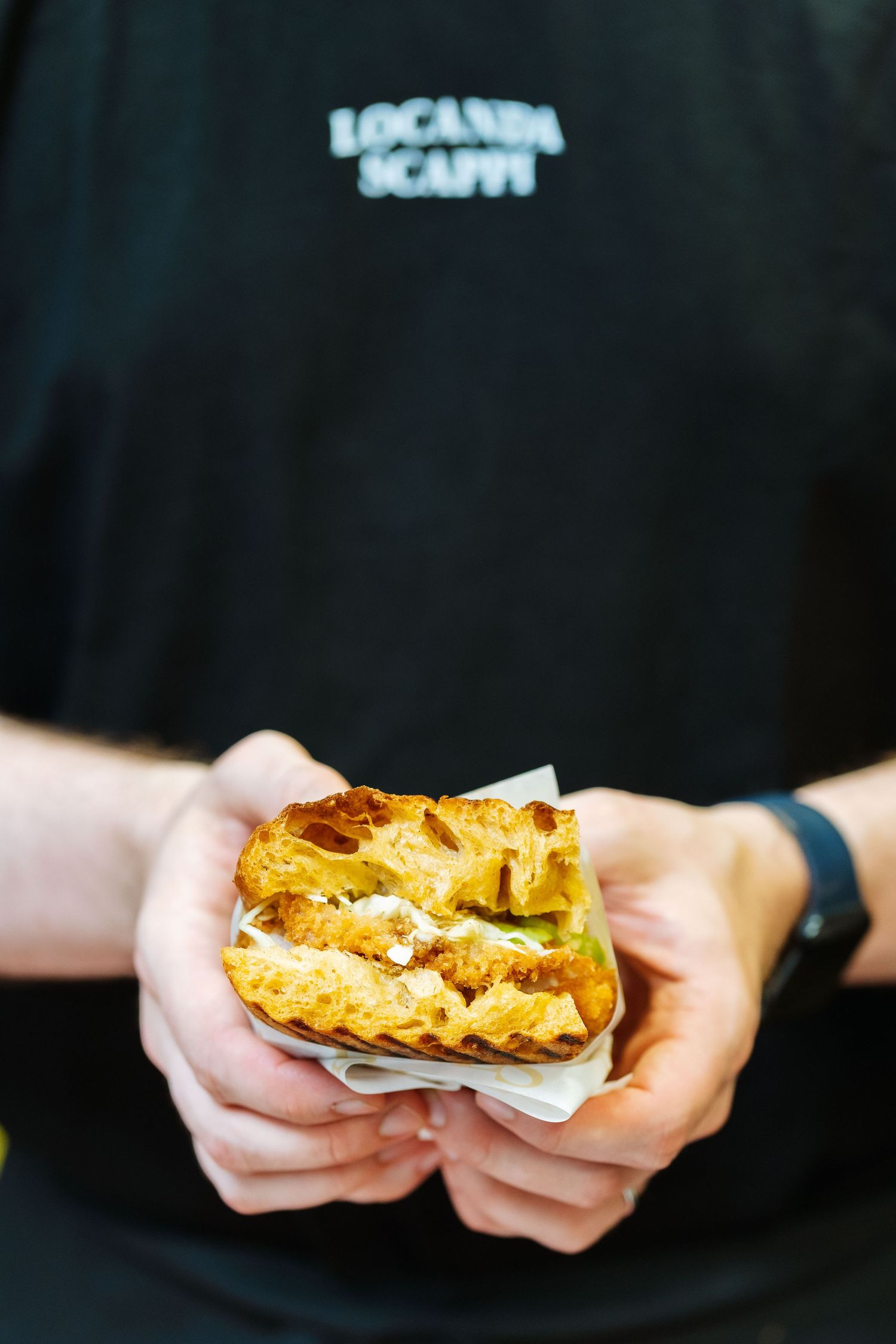 Person in Locanda Scappi black shirt holding a golden fried sandwich with both hands.
