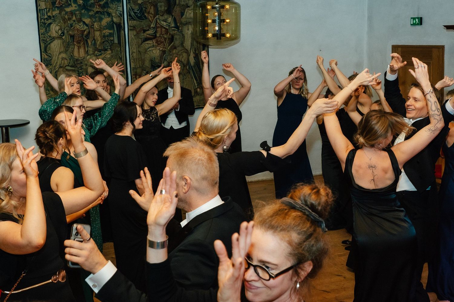 Crowd of formally dressed guests dancing with raised hands at lively gala celebration.