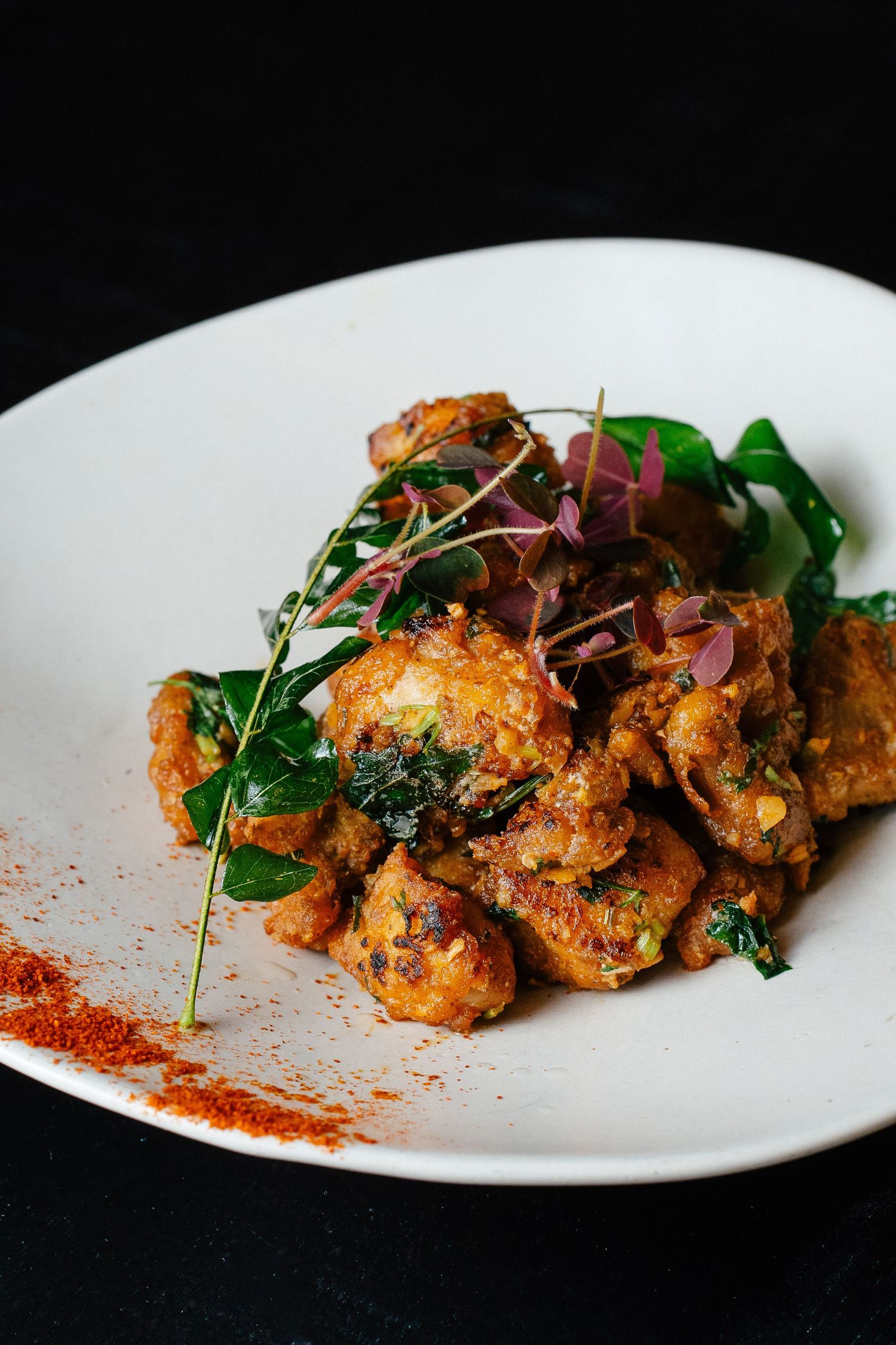 Crispy fried chicken pieces garnished with fresh greens and paprika on a white plate.