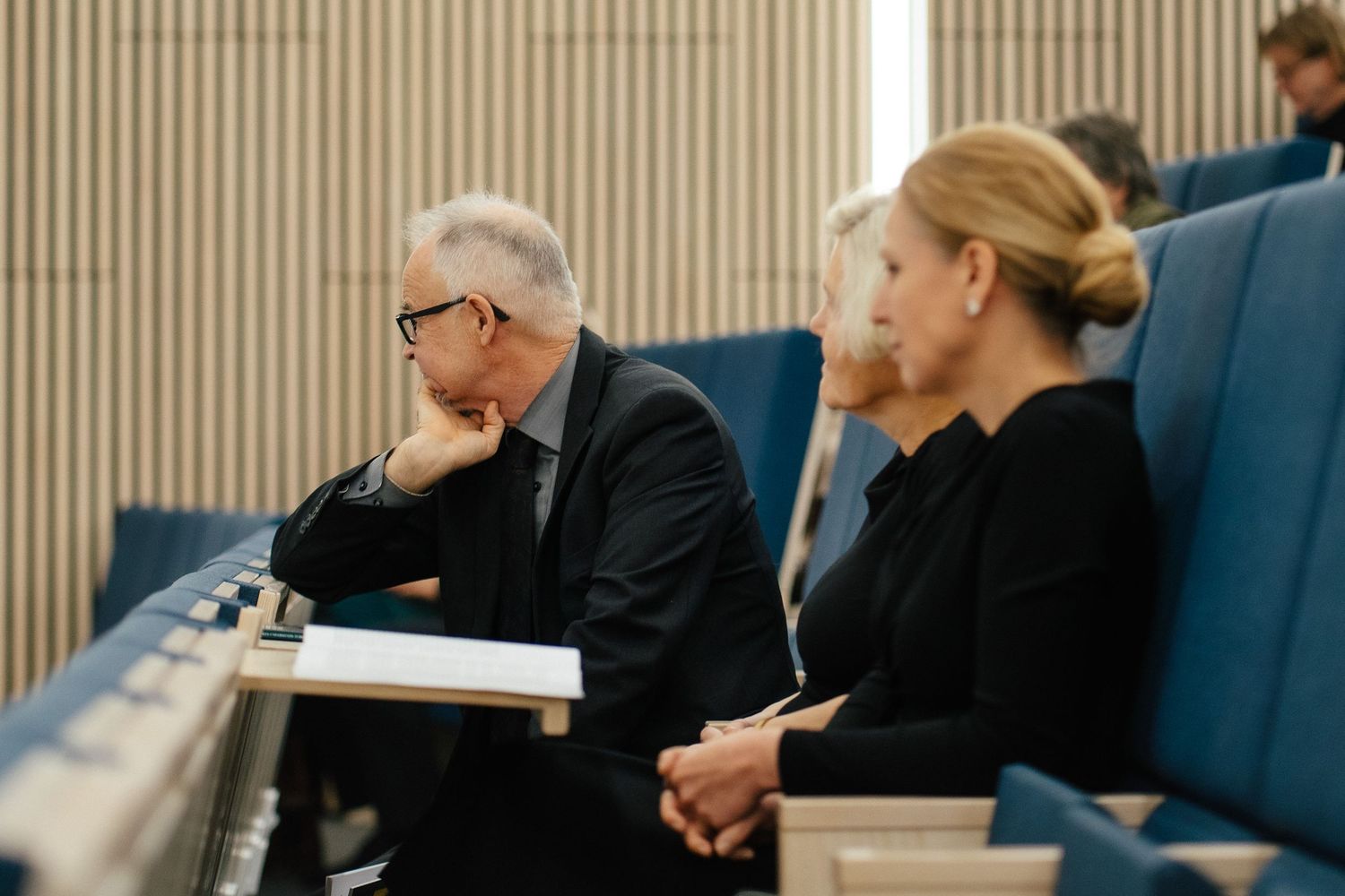 Two professionals in black attire seated in modern auditorium during a conference presentation.