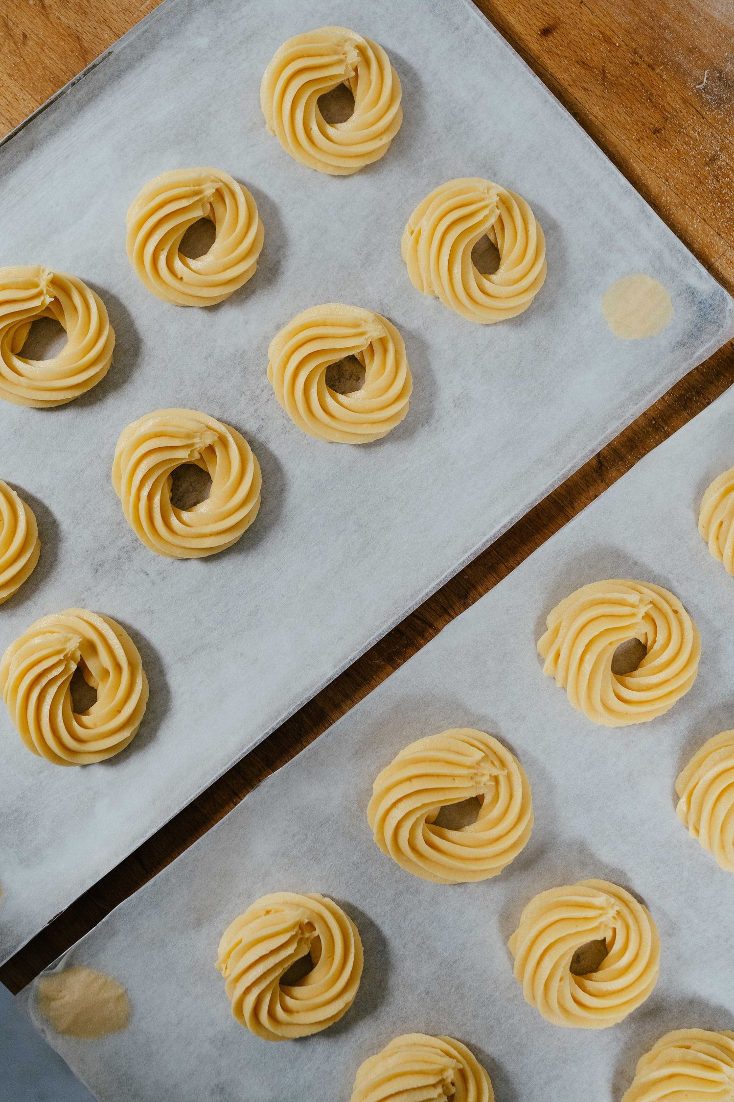 Rows of piped swirled butter cookie dough rosettes on parchment-lined baking trays ready for the oven.