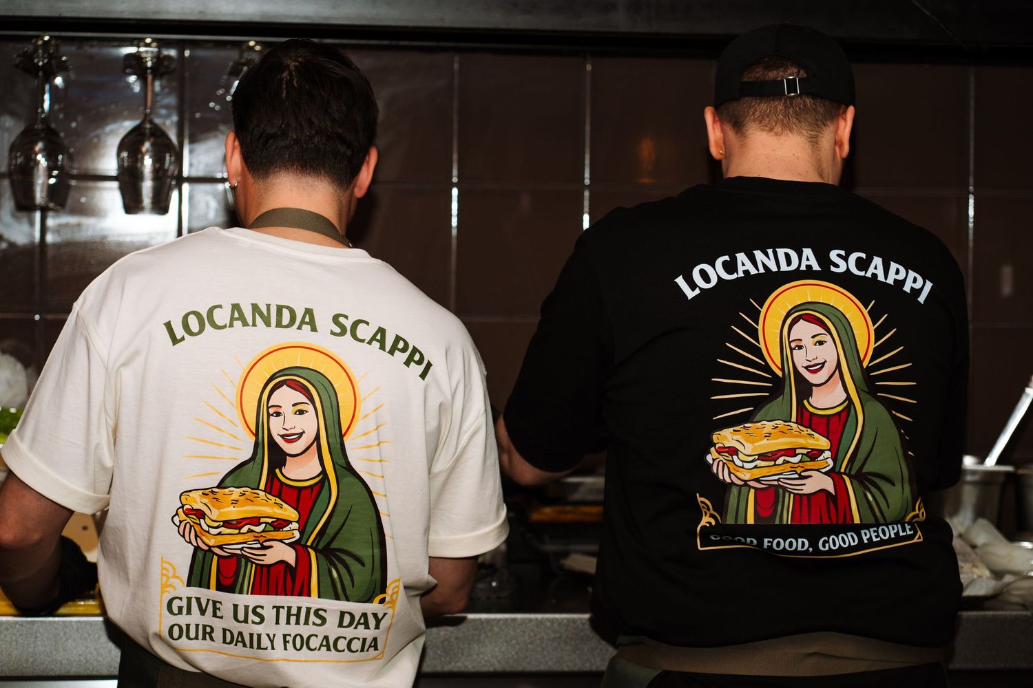 Two staff wearing Locanda Scappi shirts with Give Us This Day Our Daily Focaccia printed on back.