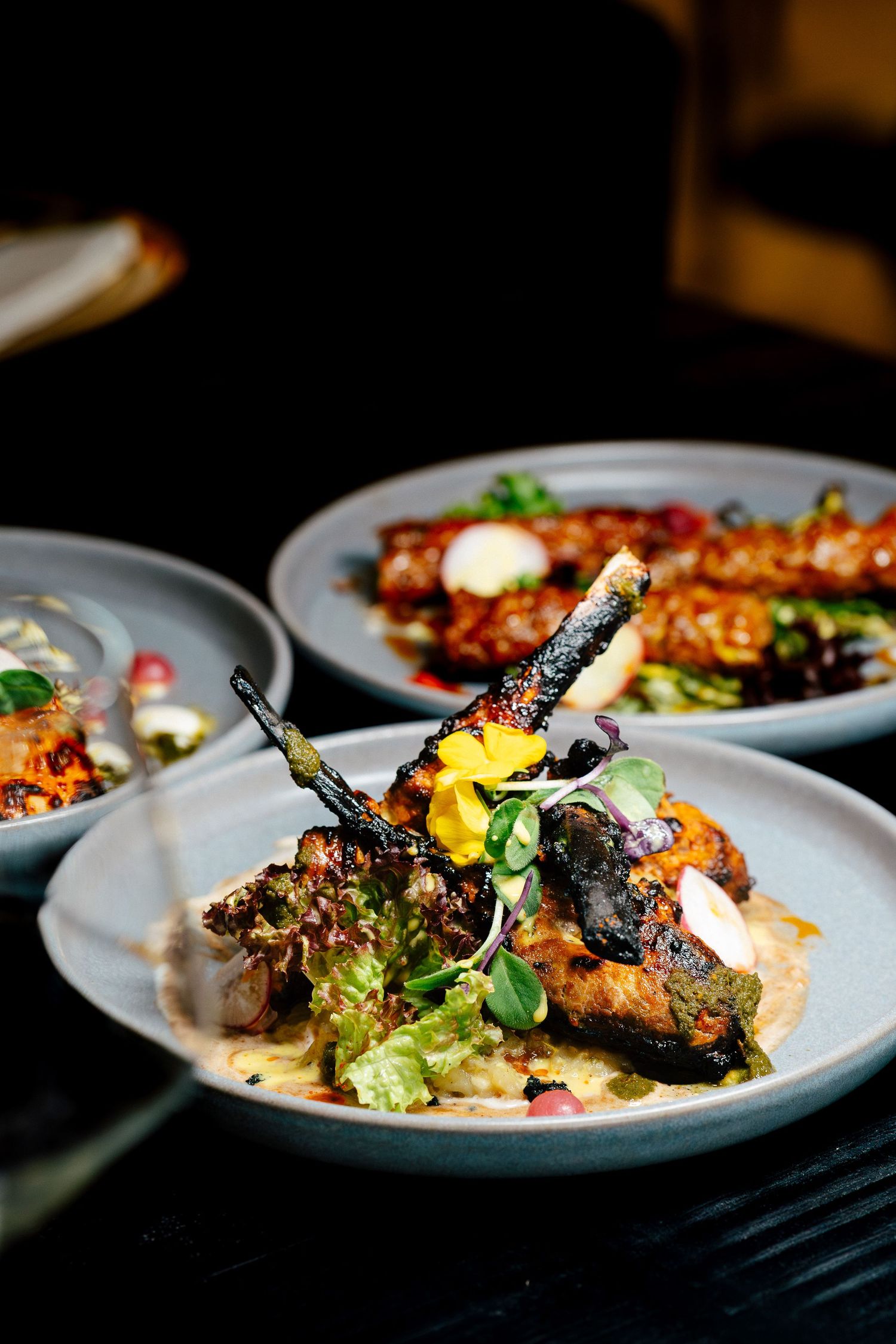 Elegantly plated grilled meat dish with fresh greens and edible flowers on a gray plate.
