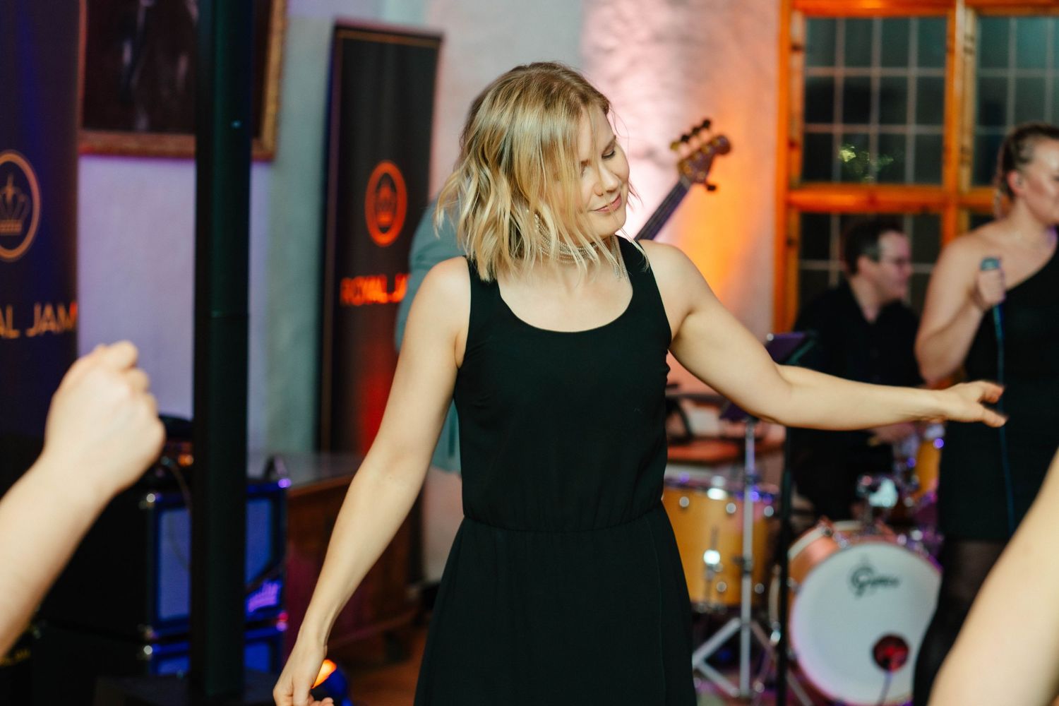 Woman in black dress dancing energetically at a live music event with band performing behind her.