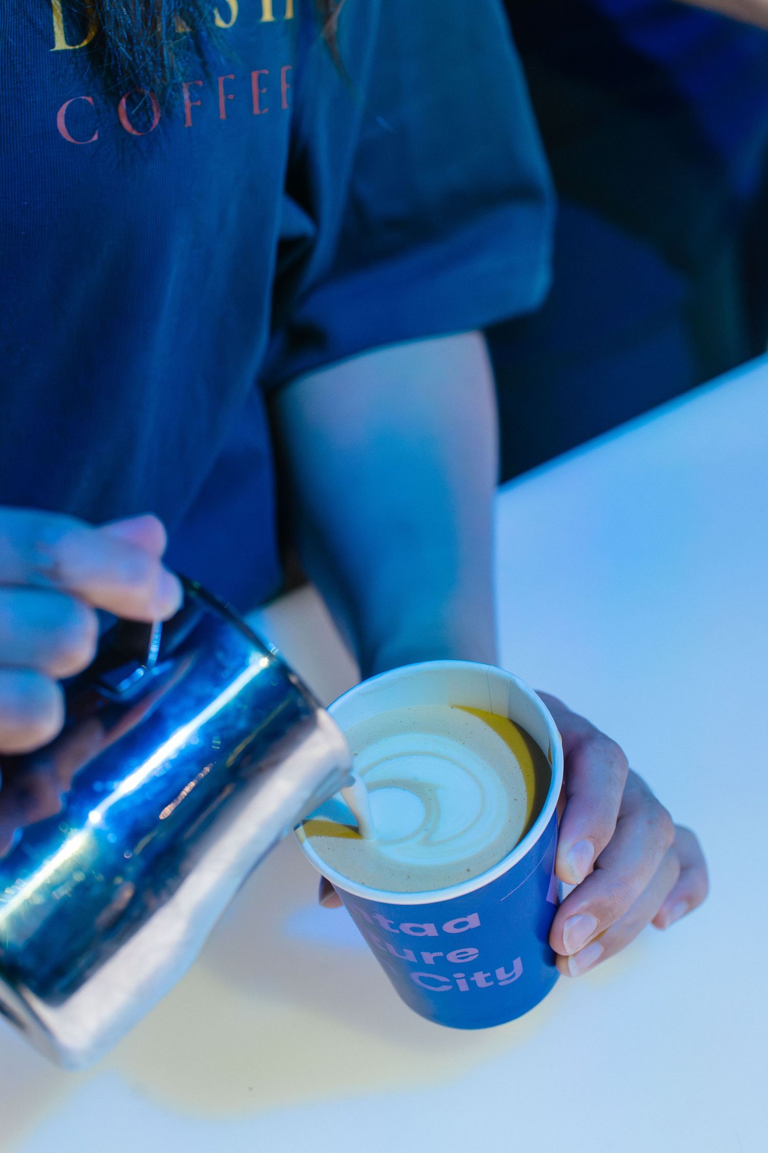 Barista pouring steamed milk into branded Vantaa Future Tech City blue cup.