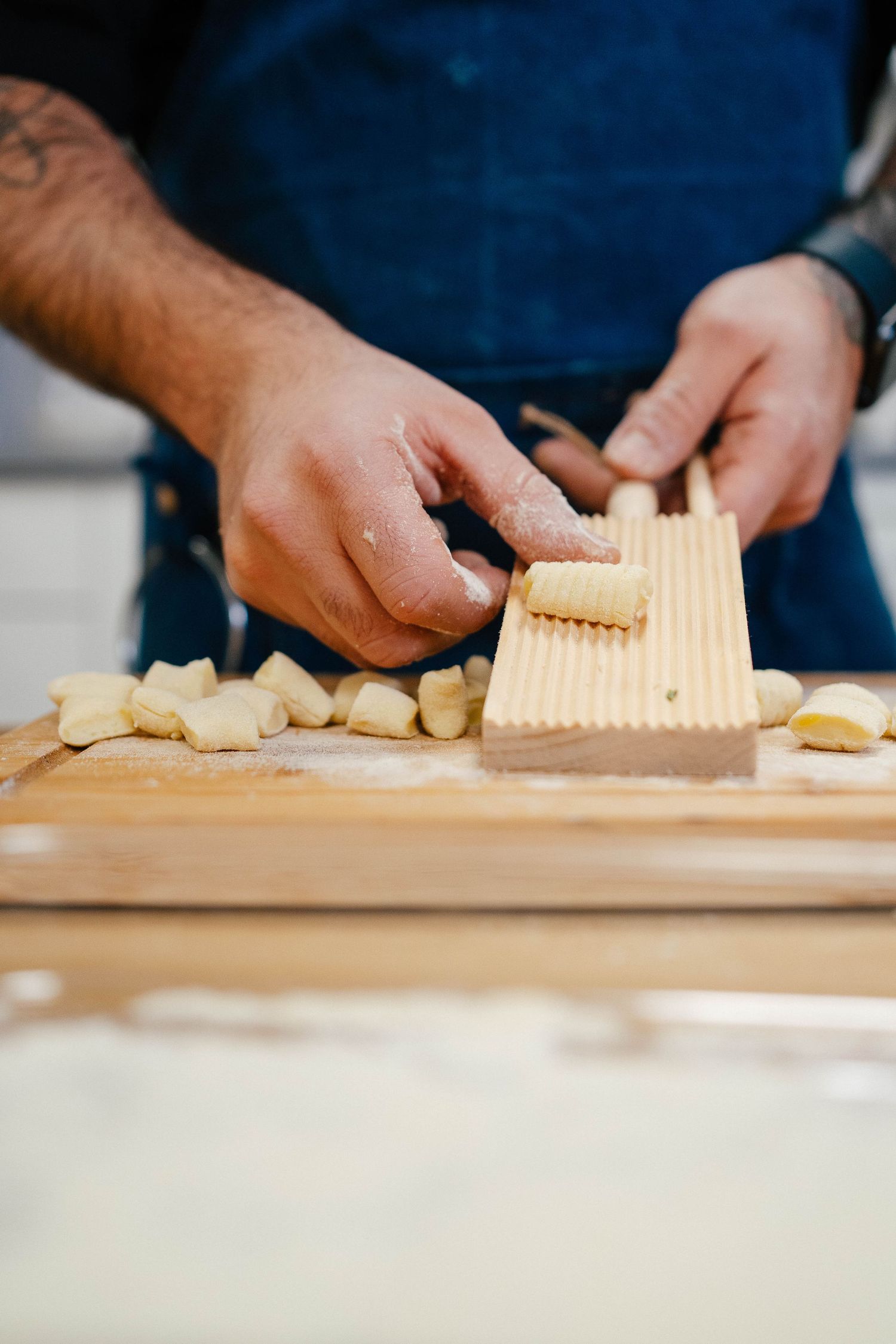 Chef shaping homemade gnocchi using a wooden ridged board on a floured surface.
