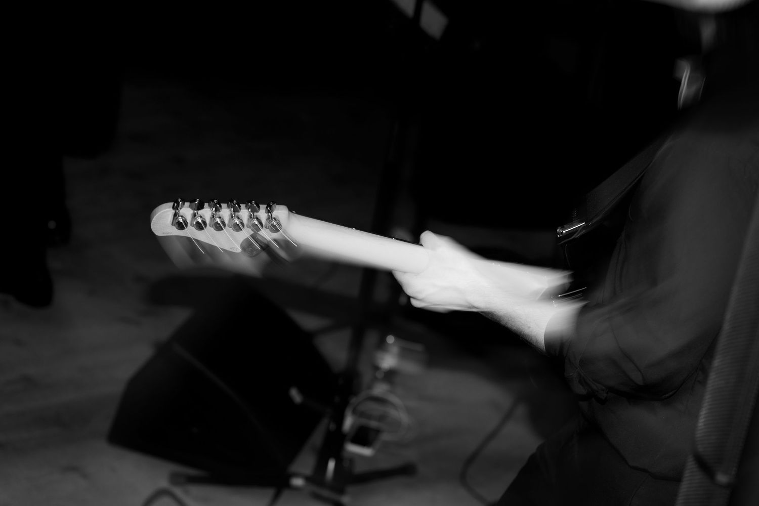 Black and white close-up of guitarist holding electric guitar neck during live performance.
