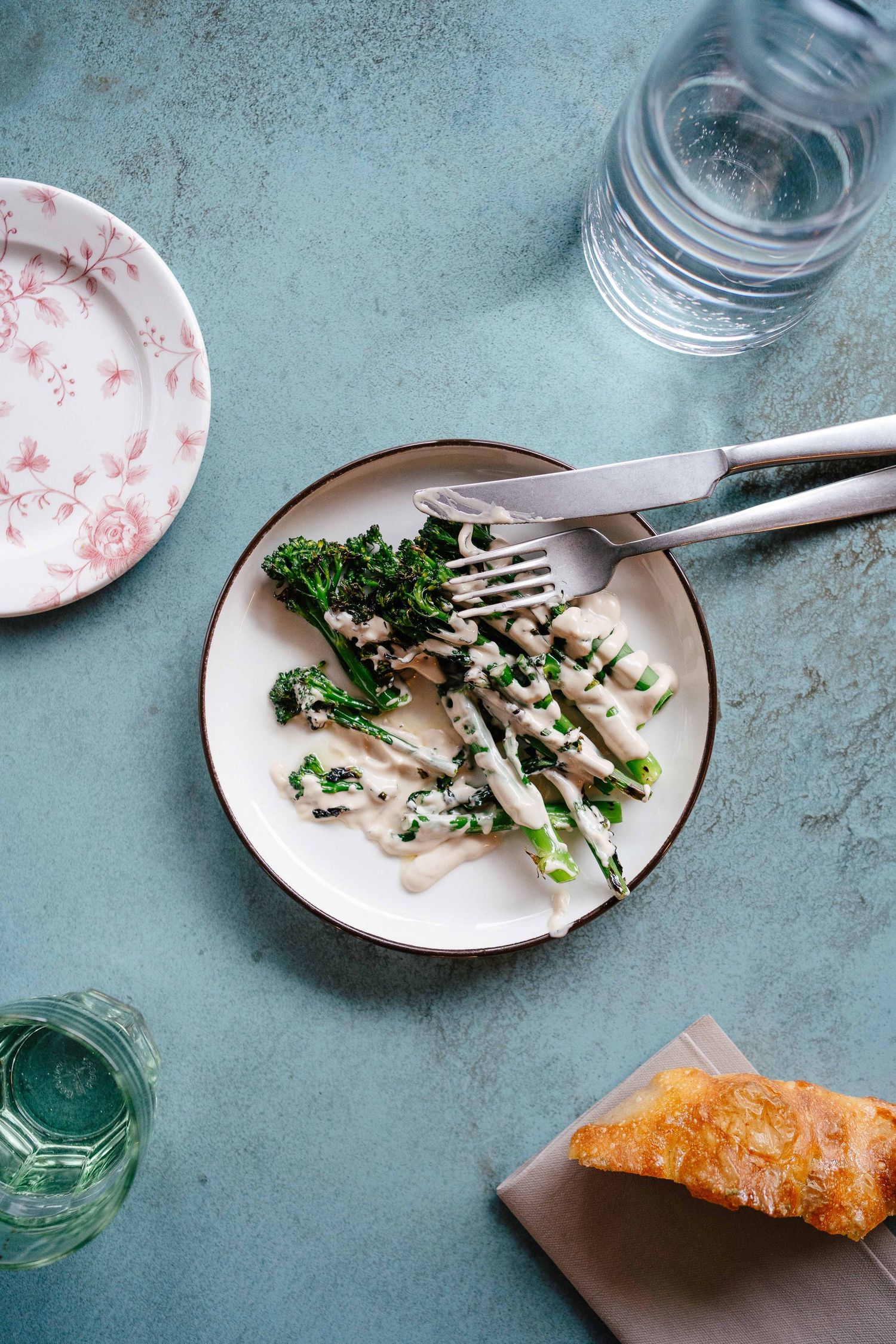 Plate of gnocchi with kale and cream sauce, fork and knife resting on plate, bread and water glasses nearby.